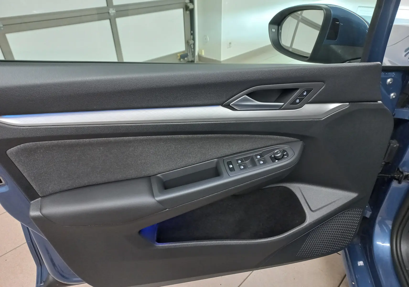 Vue rapprochée de la porte avant gauche de la Volkswagen Golf Bleu Anemone avec commandes électriques et garniture noire.