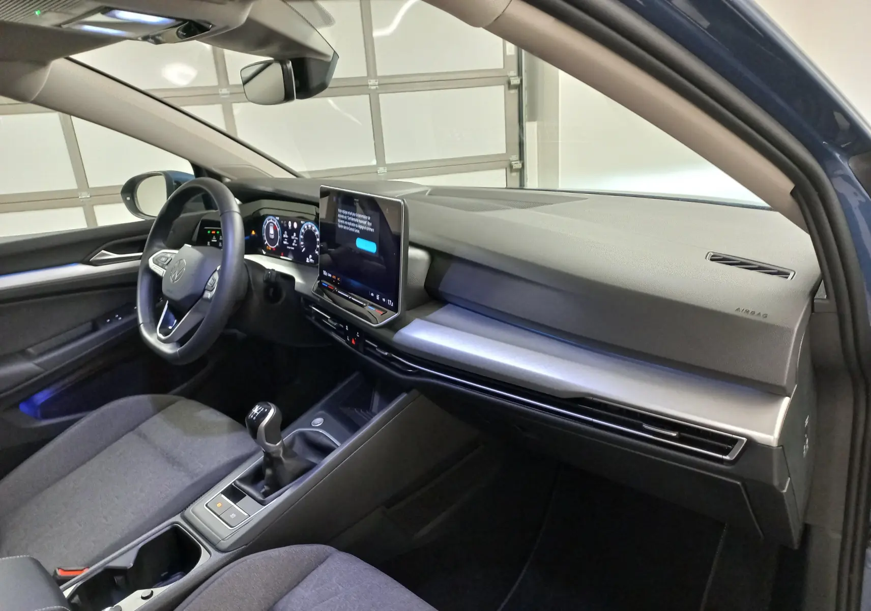 Intérieur avant droit de la Volkswagen Golf 1.5 TSI 116 BVM6 VW Edition 2025, tableau de bord moderne et levier de vitesses manuel visible.