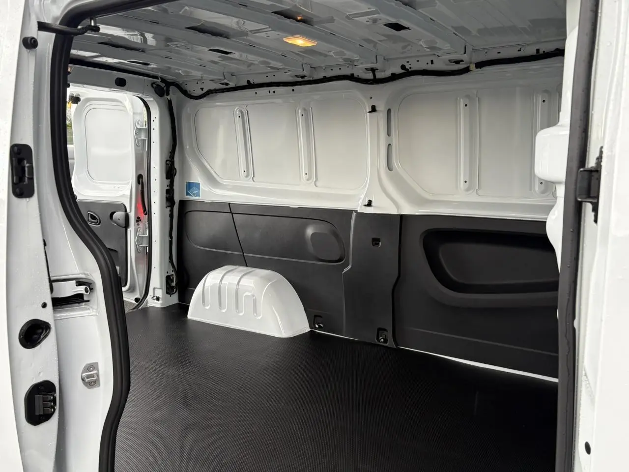 Intérieur du Renault Trafic Fourgon blanc Glacier vu de l’arrière, montrant le plancher bois et la cloison tôlée.