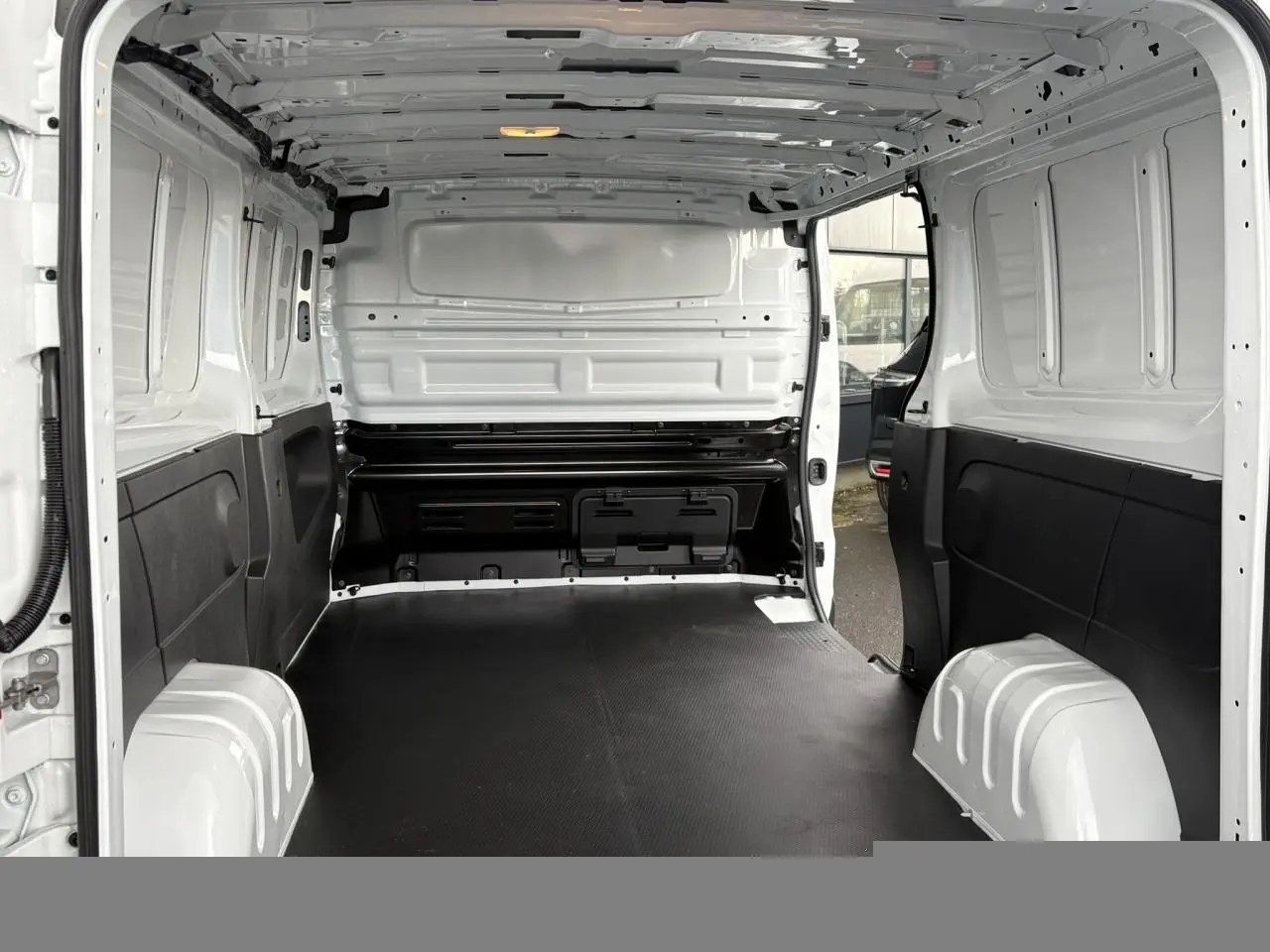 Vue intérieure arrière du Renault Trafic Fourgon blanc Glacier, montrant l'espace de chargement avec plancher bois noir et parois blanches.