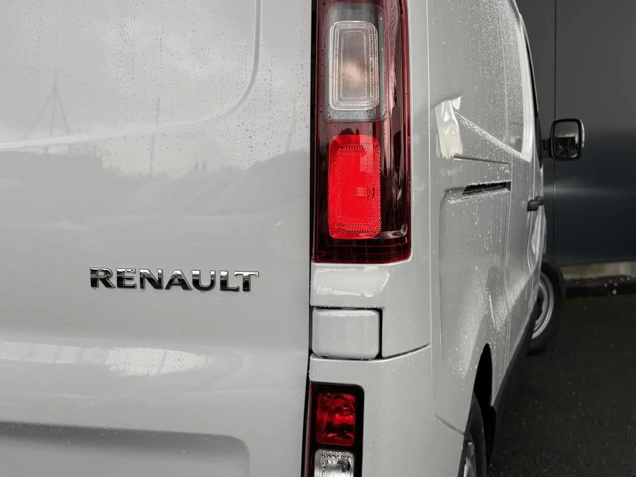 Vue arrière droite du Renault Trafic Fourgon blanc Glacier avec feux arrière verticaux et logo Renault visible.