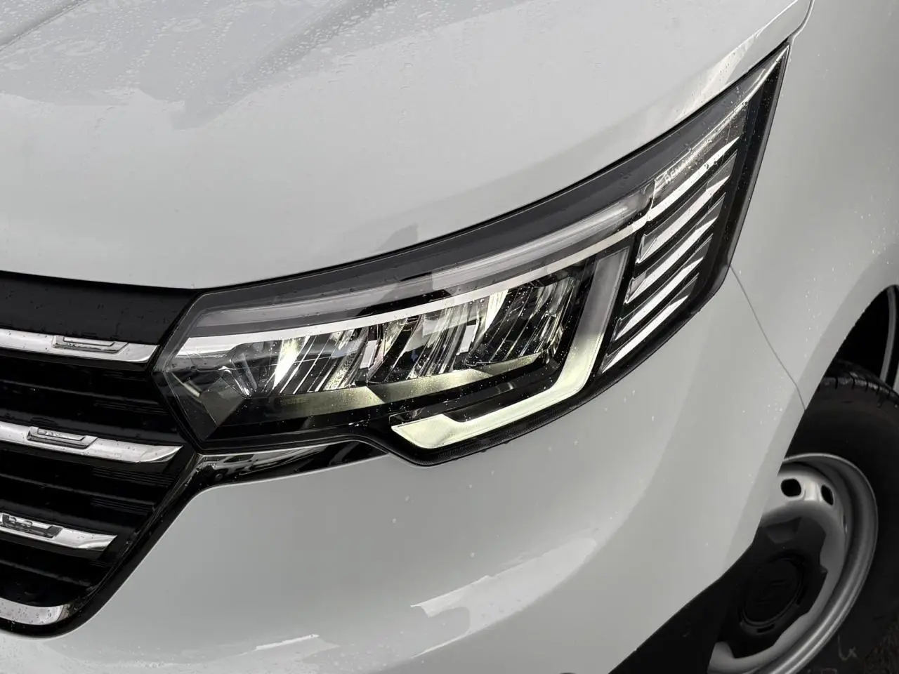 Gros plan sur le phare avant droit LED du Renault Trafic Fourgon blanc Glacier avec calandre noire et jante acier.