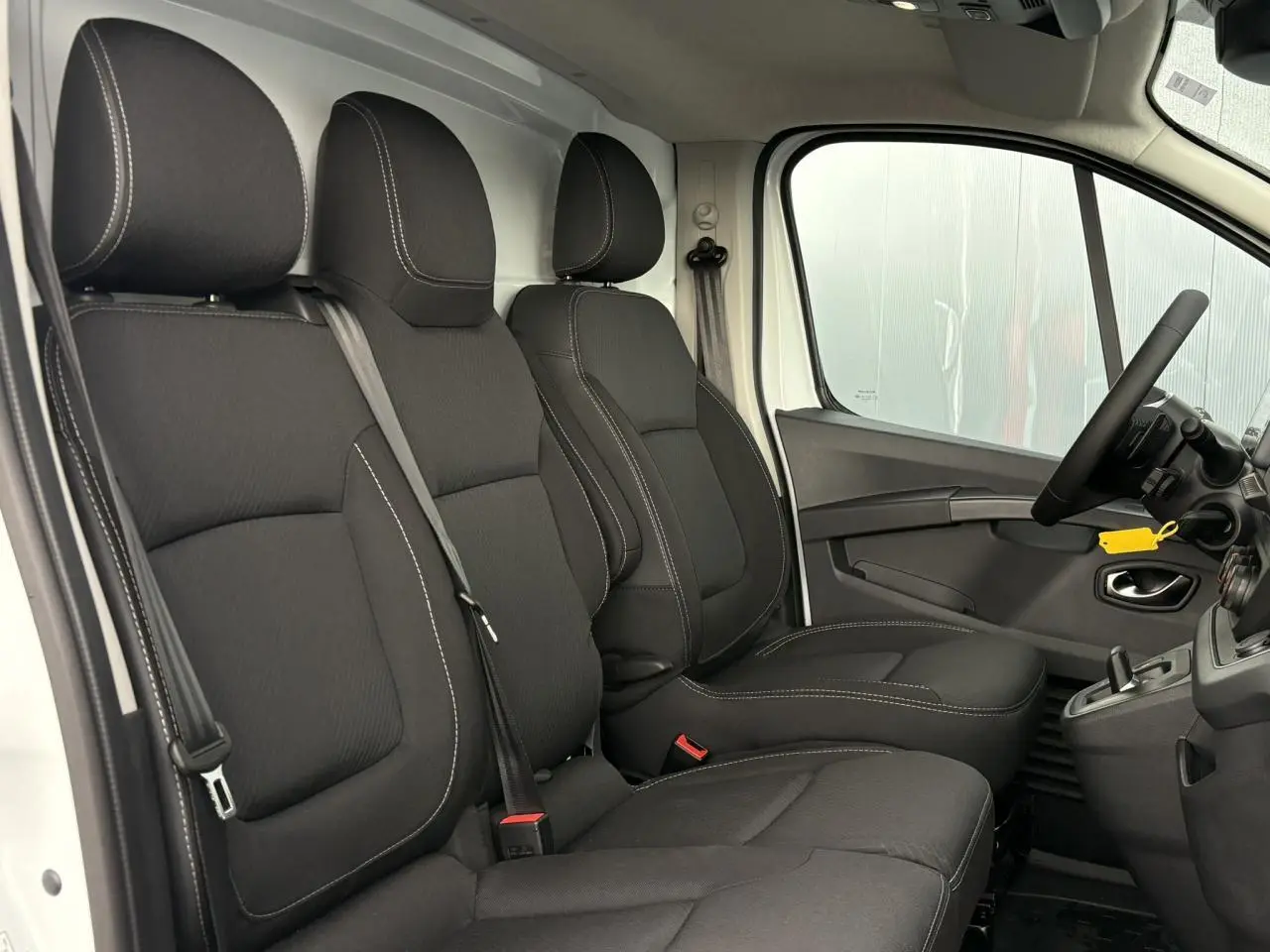 Vue intérieure côté conducteur du Renault Trafic Fourgon blanc, sièges tissu noir avec coutures contrastantes.