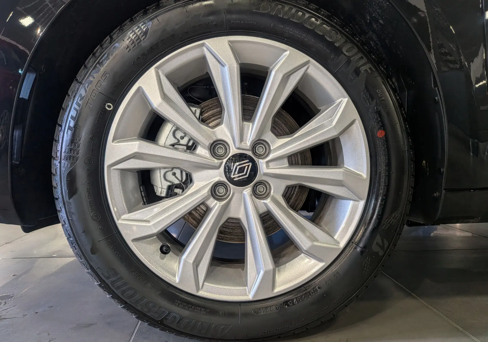 Gros plan sur la roue avant gauche de la Renault Clio V noire, mettant en valeur la jante alliage argentée au design moderne.