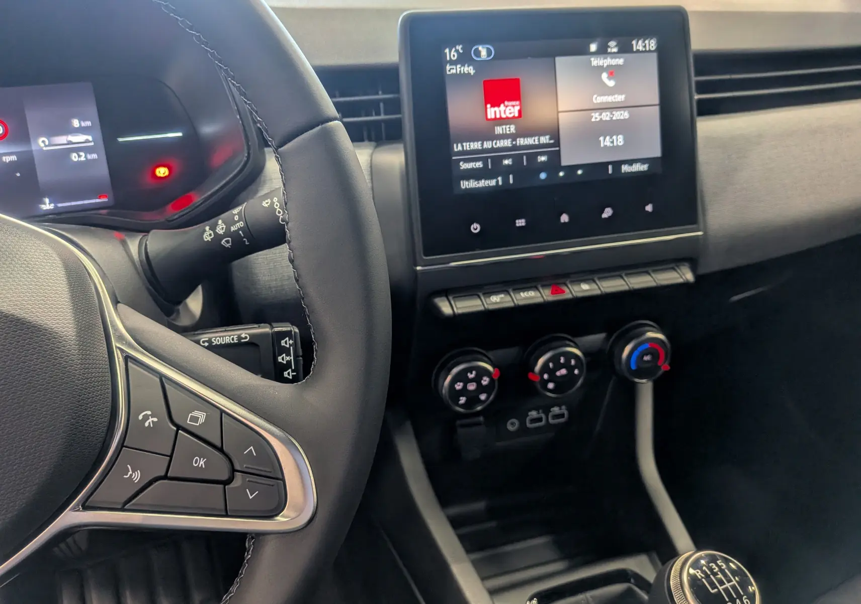Vue intérieure centrée sur le volant et la console centrale d'une Renault Clio V noire, avec écran tactile et boîte manuelle.