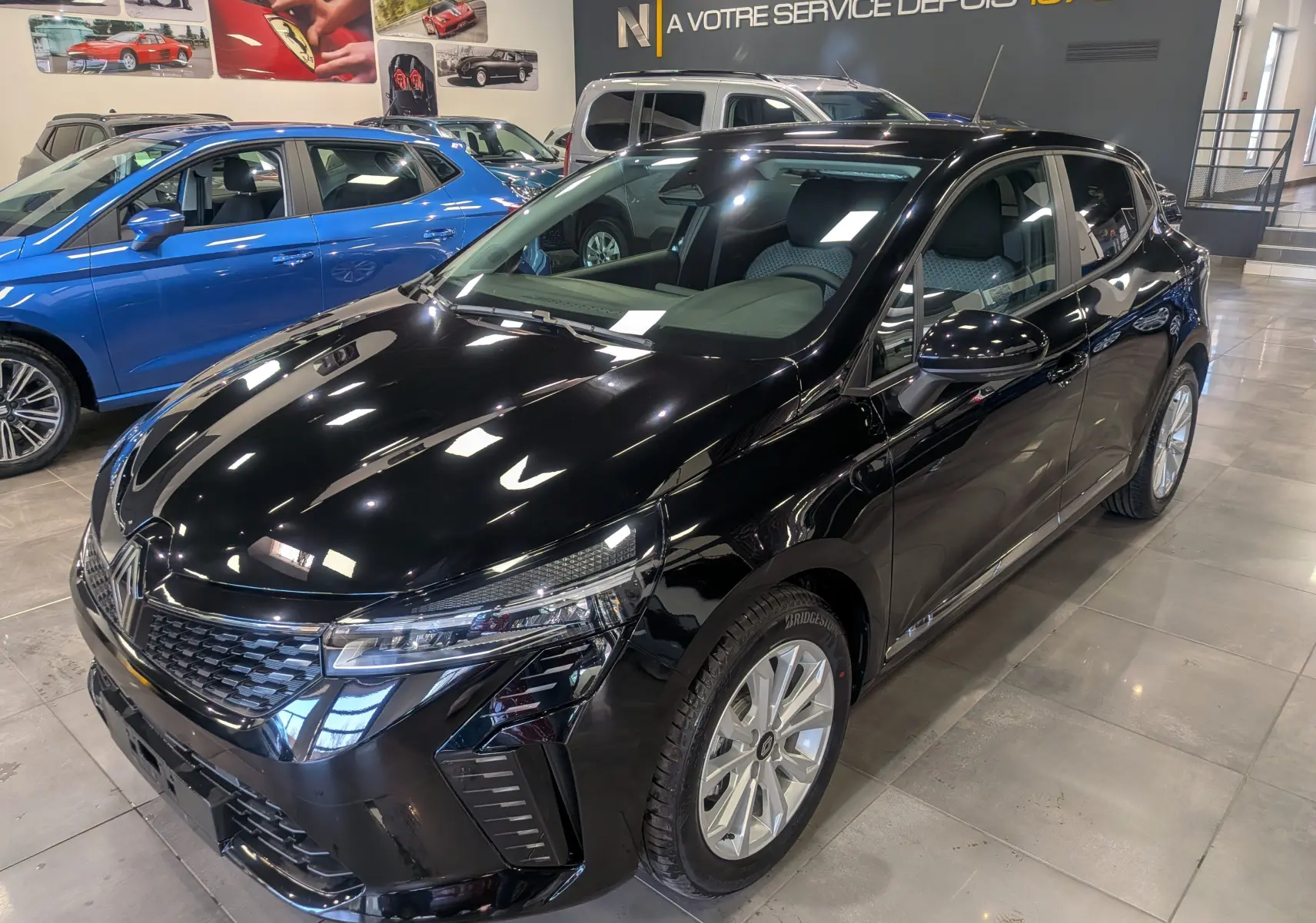 Renault Clio V noire vue en 3/4 avant droit dans un showroom, avec jantes argentées et phares LED distinctifs.