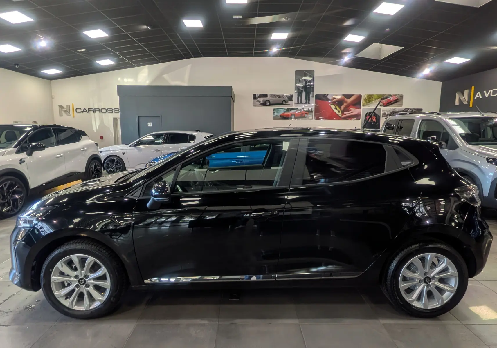 Profil côté gauche d'une Renault Clio V noire 2025 en intérieur, mettant en valeur sa silhouette compacte et ses lignes modernes.