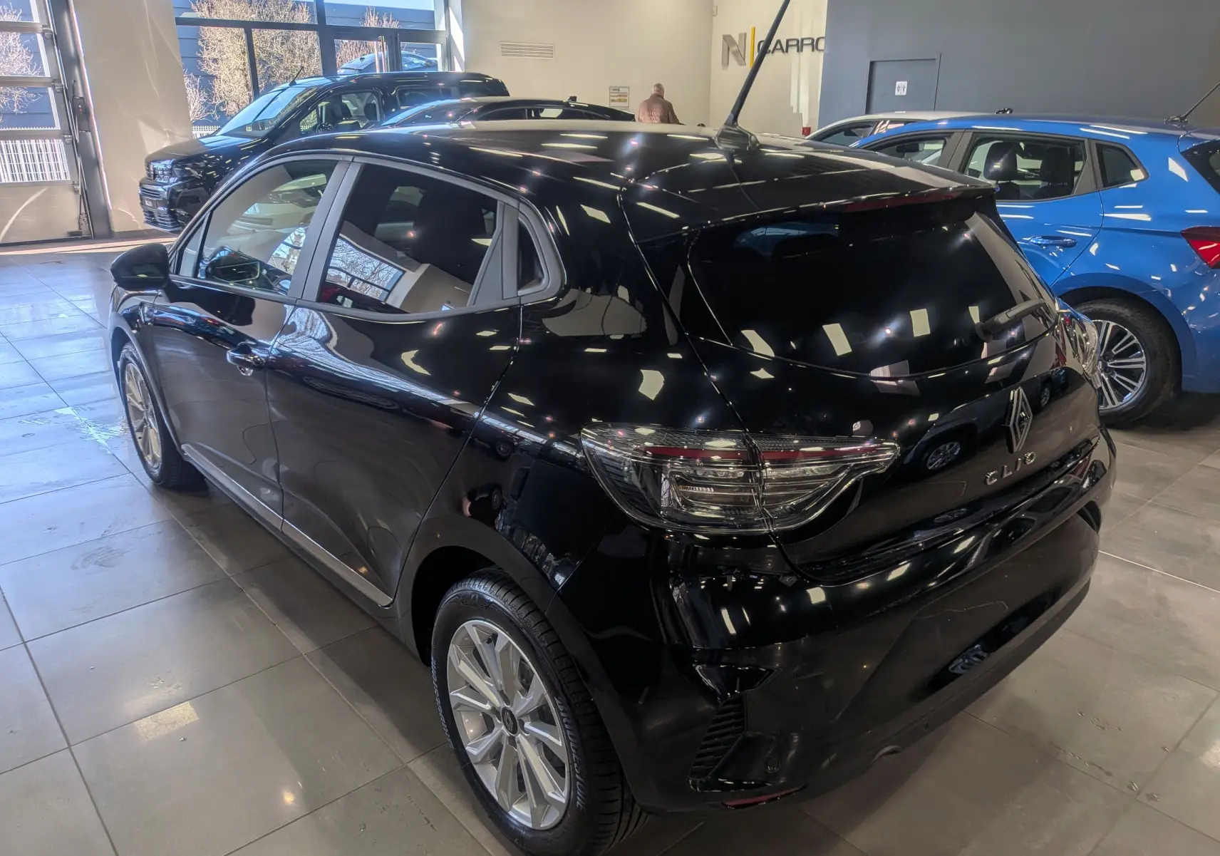 Vue 3/4 arrière droite d'une Renault Clio V noire 2025 en intérieur, avec feux arrière LED et jantes alliage visibles.