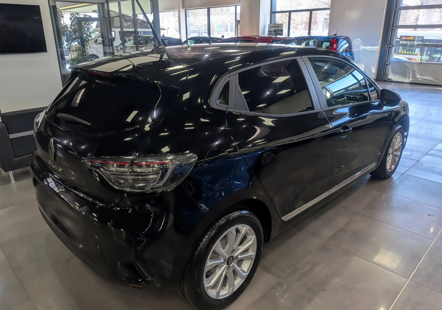 Vue 3/4 arrière droite d'une Renault Clio V noire 2025 en showroom, avec jantes alliage et vitres teintées.