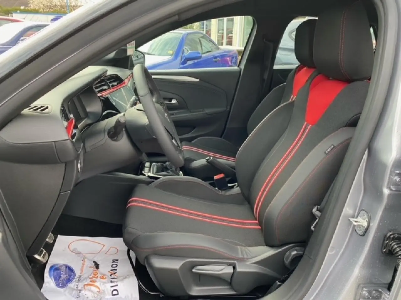 Vue intérieure côté conducteur de l’Opel Corsa gris magnetic 2022, sièges tissu noir et rouge avec surpiqûres rouges.