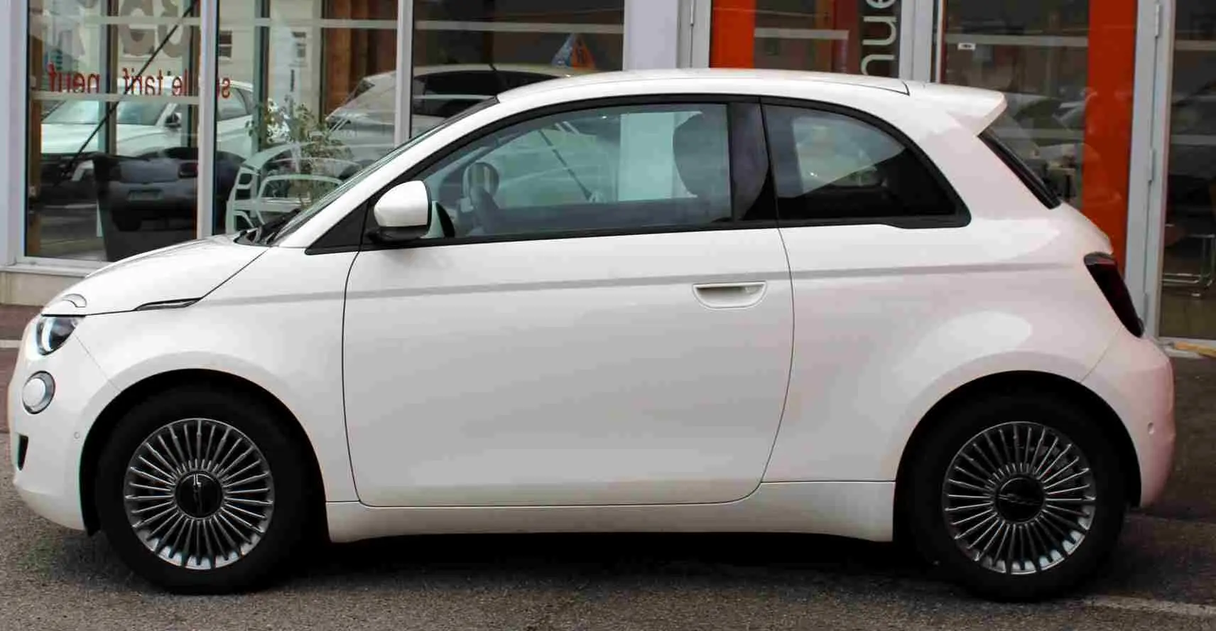 Profil côté gauche de la Fiat 500 électrique blanche 2023, avec jantes spécifiques et lignes arrondies distinctives.
