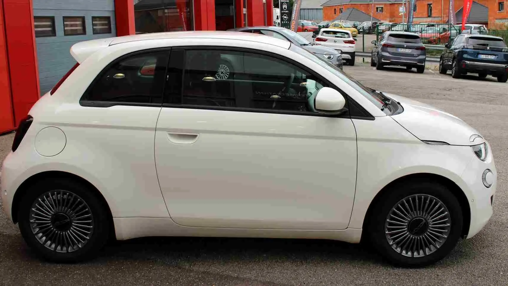 Profil côté gauche de la Fiat 500 électrique blanche 2023, avec jantes spécifiques et rétroviseurs assortis.