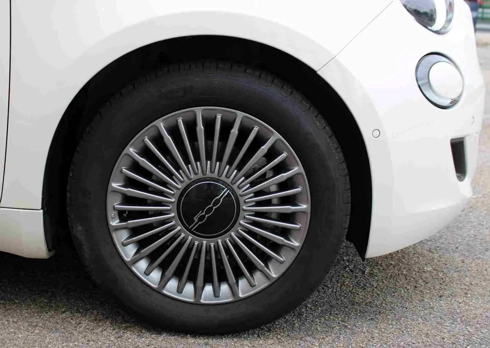 Gros plan sur la roue avant gauche de la FIAT 500 électrique blanche, avec jante au design rayonné argenté.