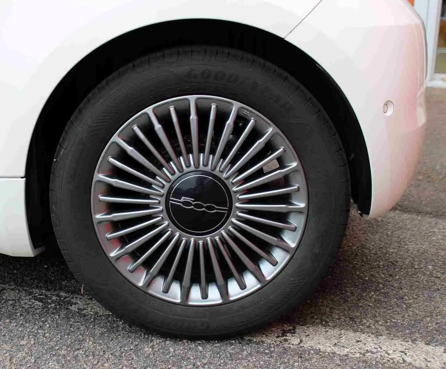 Gros plan sur la roue avant droite d'une FIAT 500 électrique blanche, avec jante multibranches argentée et logo central 500.
