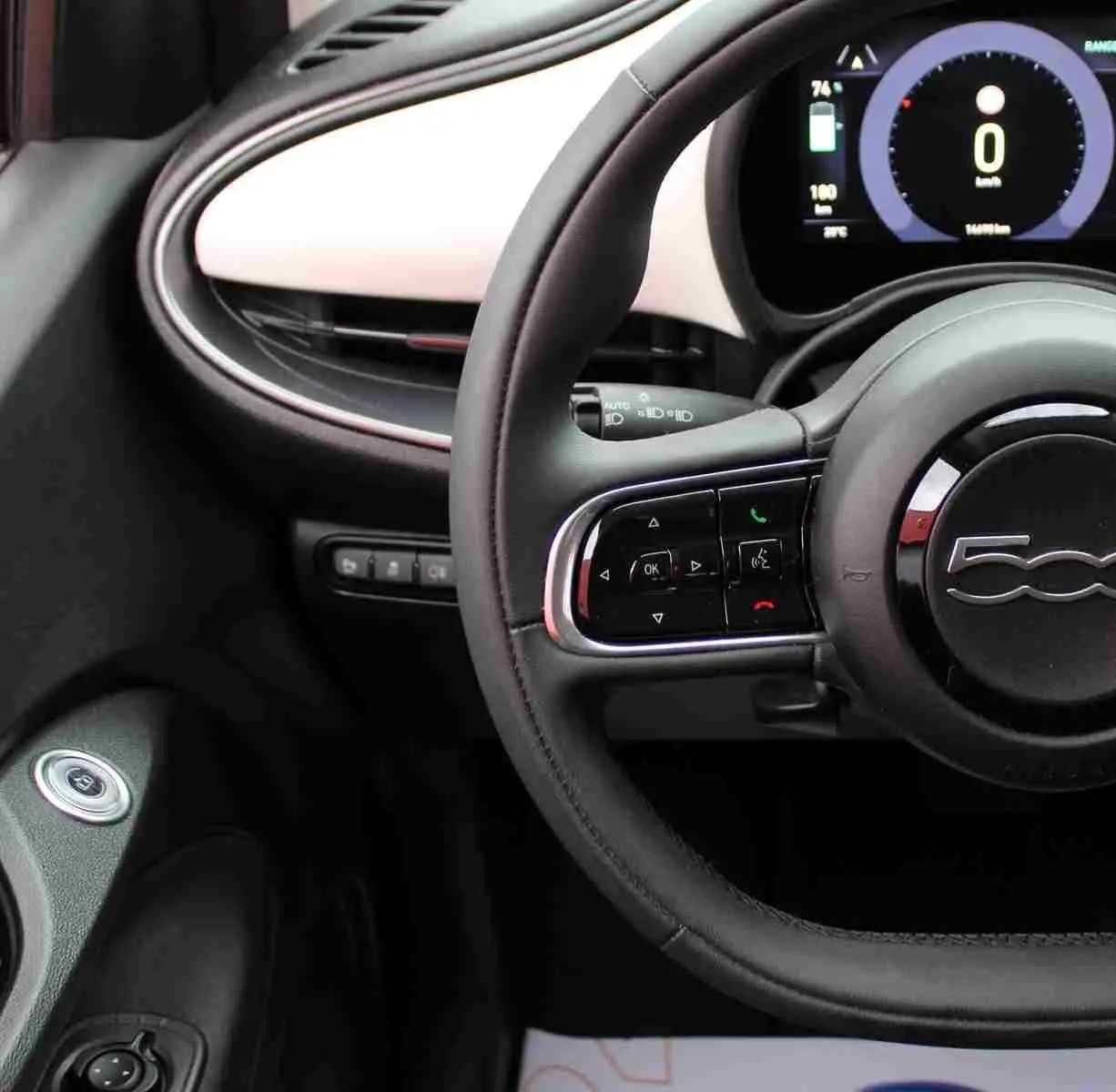 Vue rapprochée du volant noir et du tableau de bord blanc de la Fiat 500 électrique 2023 avec affichage numérique.
