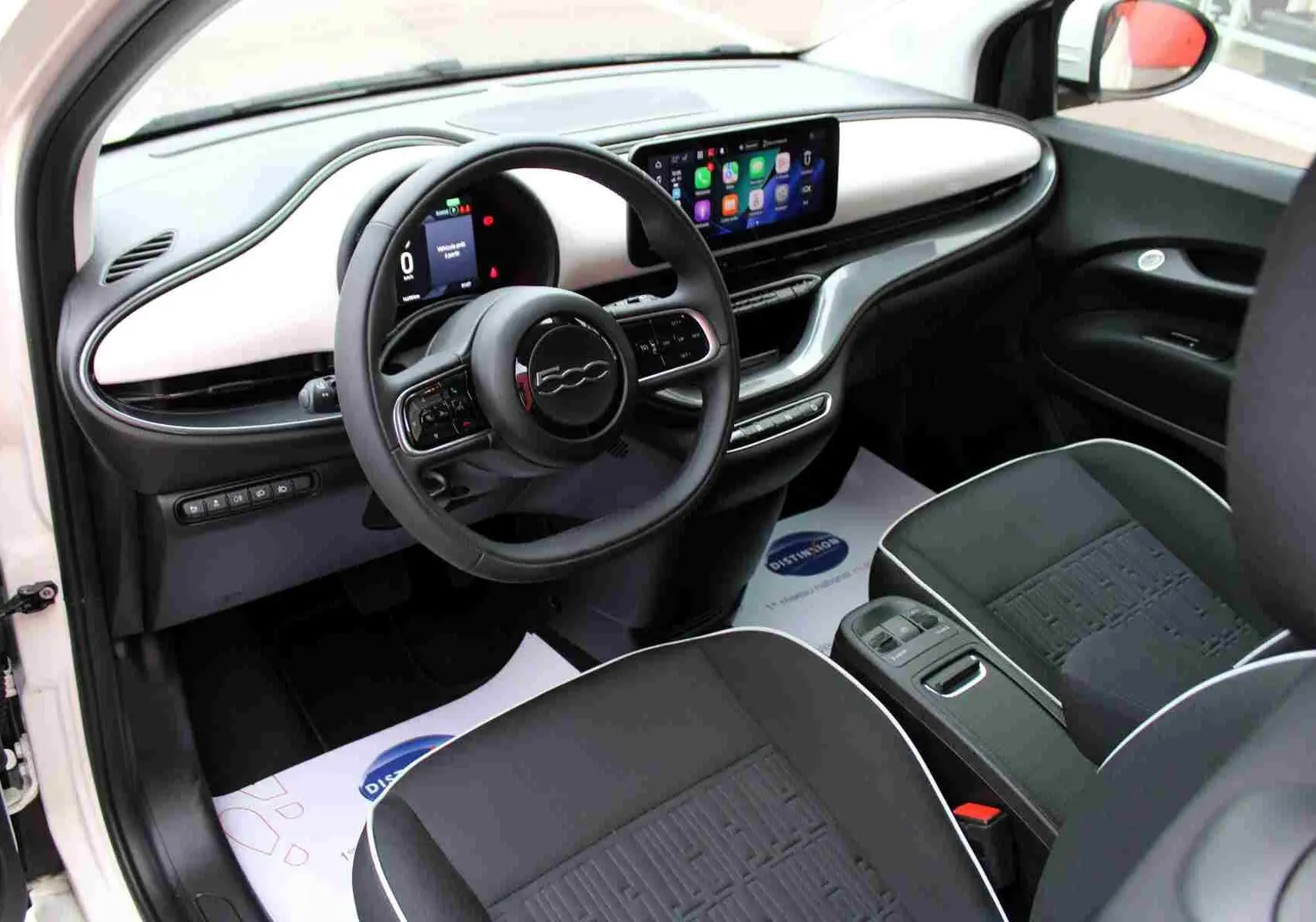 Intérieur de la FIAT 500 électrique 2023 vu côté conducteur, tableau de bord blanc et écran tactile avec CarPlay.
