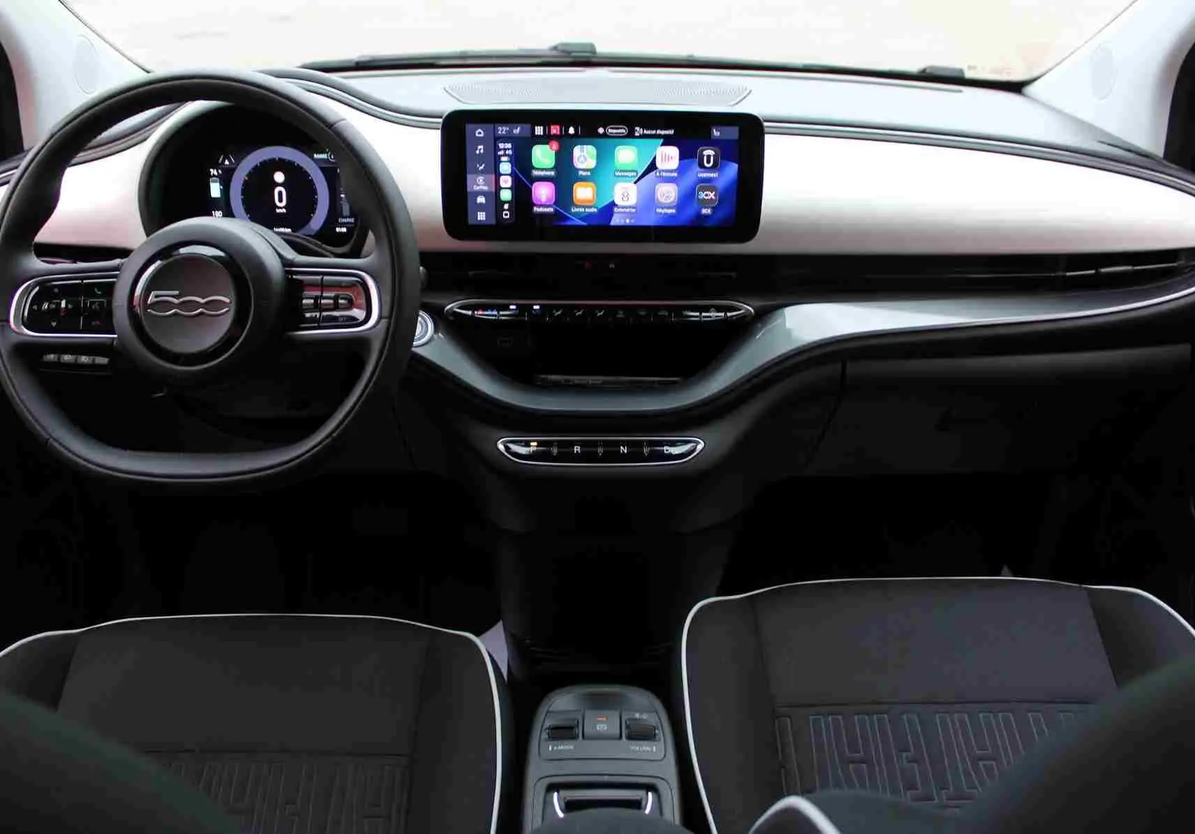 Vue intérieure frontale du tableau de bord de la Fiat 500 électrique blanche avec écran tactile et volant multifonction.
