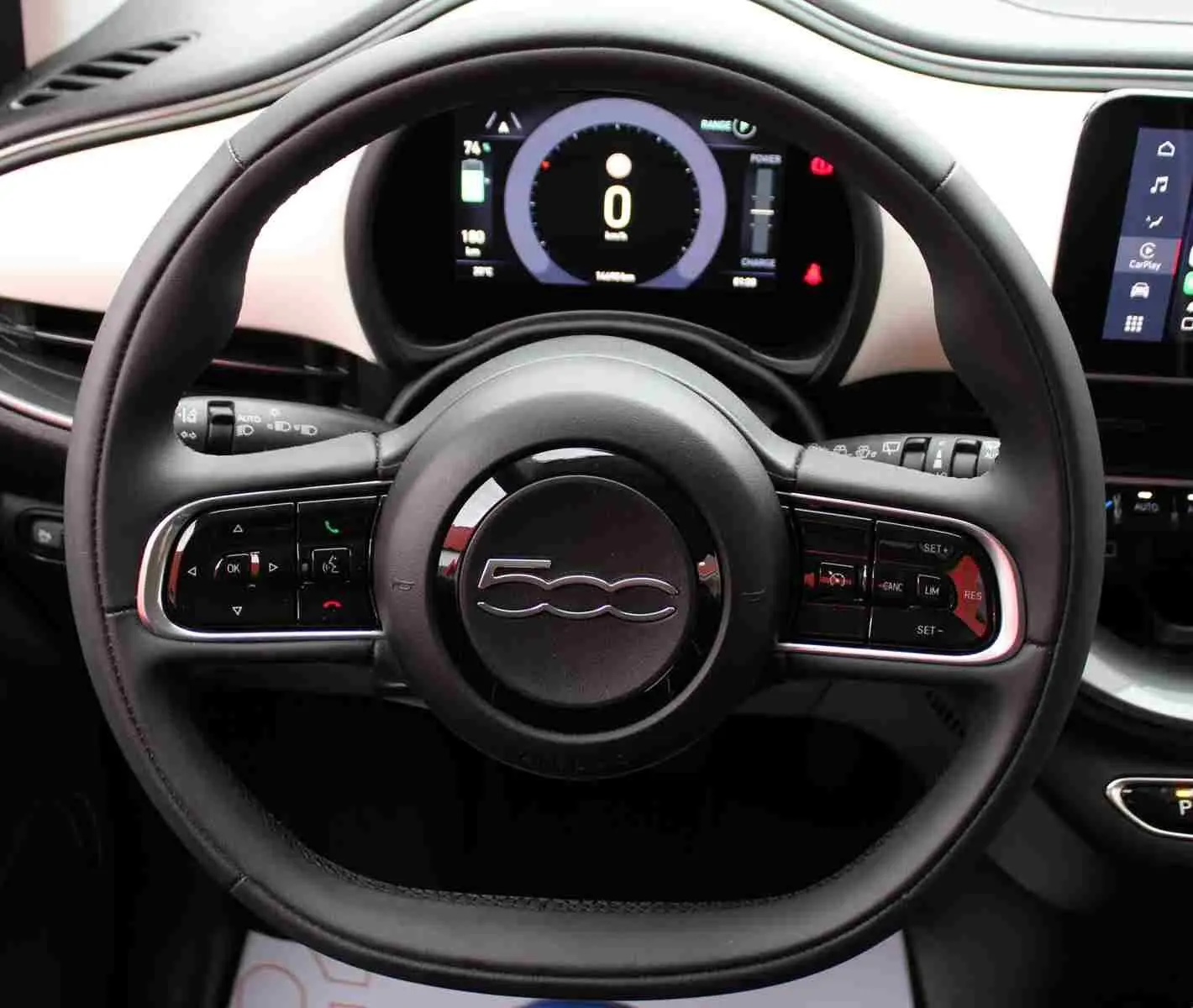 Vue rapprochée du volant noir de la Fiat 500 électrique 2023 avec tableau de bord numérique et écran tactile CarPlay.