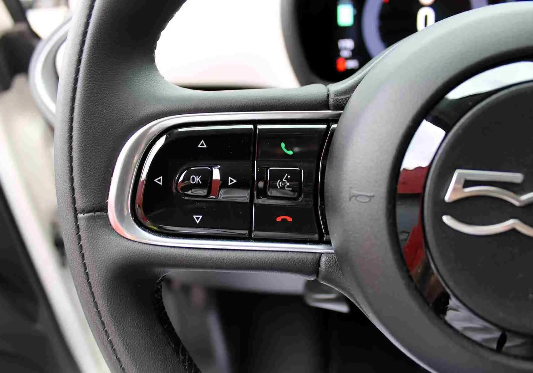 Gros plan sur les commandes à gauche du volant noir de la Fiat 500 électrique blanche, avec logo 500 visible.