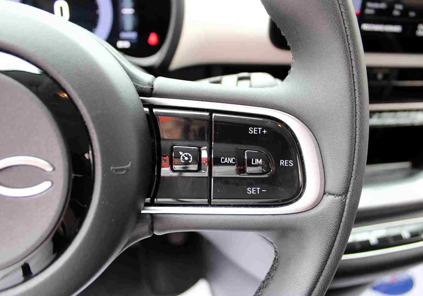 Gros plan sur les commandes de régulateur de vitesse au volant noir de la Fiat 500 électrique blanche 2023.