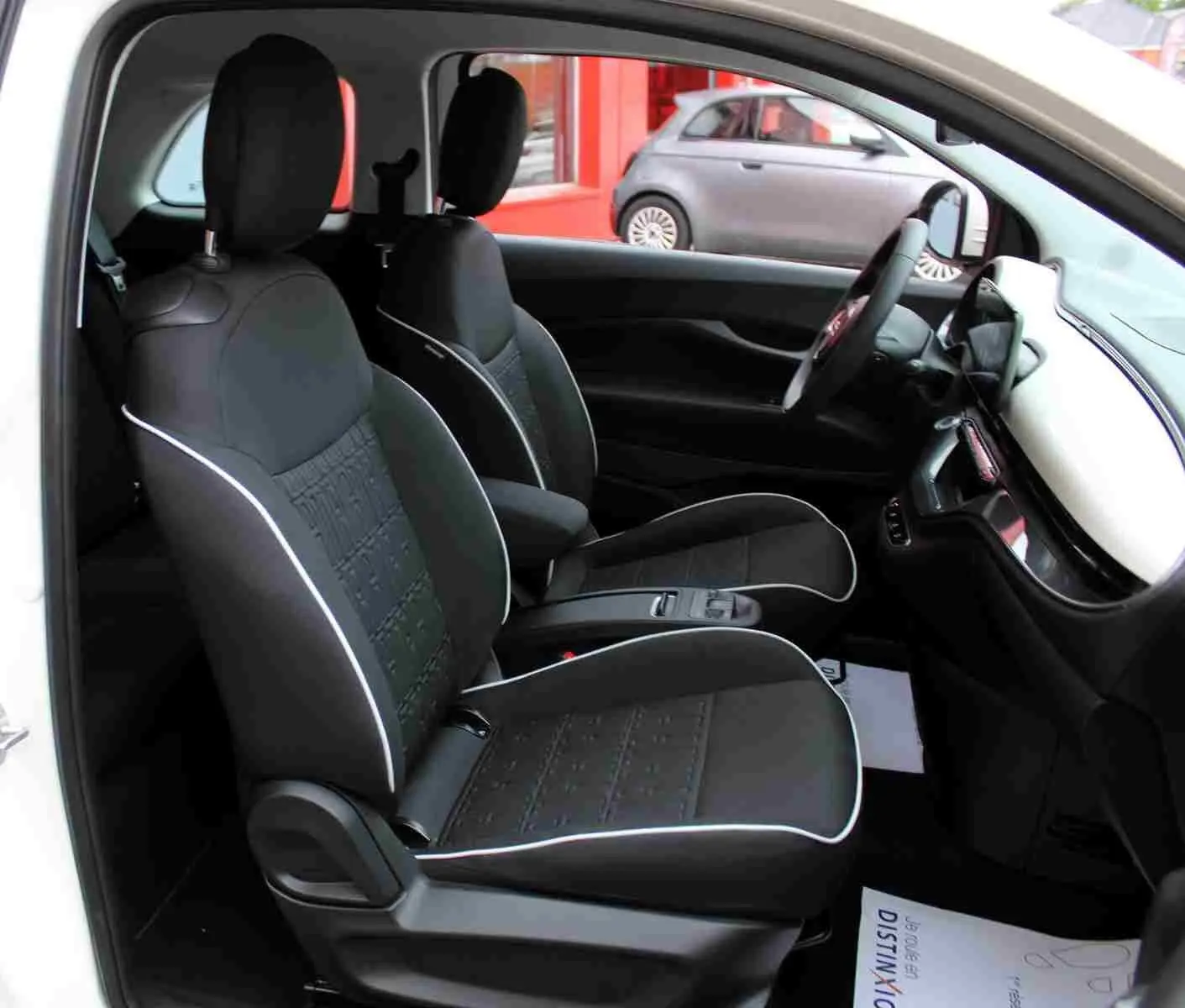 Vue intérieure côté gauche de la FIAT 500 électrique blanche 2023, montrant les sièges noirs avec surpiqûres blanches et le tableau de bord.