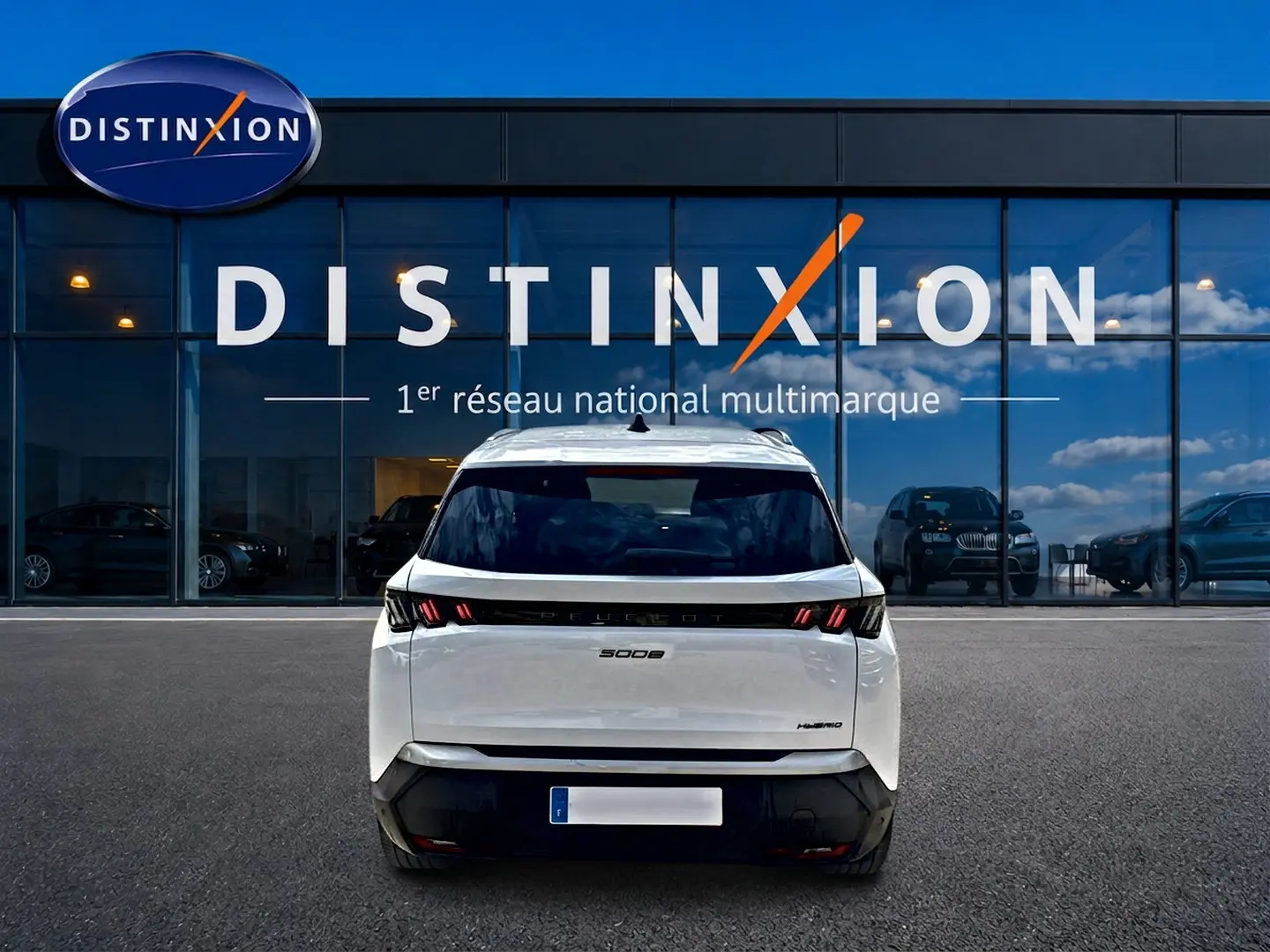 Vue arrière d’un Peugeot 5008 Hybrid blanc 2025 avec feux LED et lunette arrière surteintée devant une vitrine Distinxion.