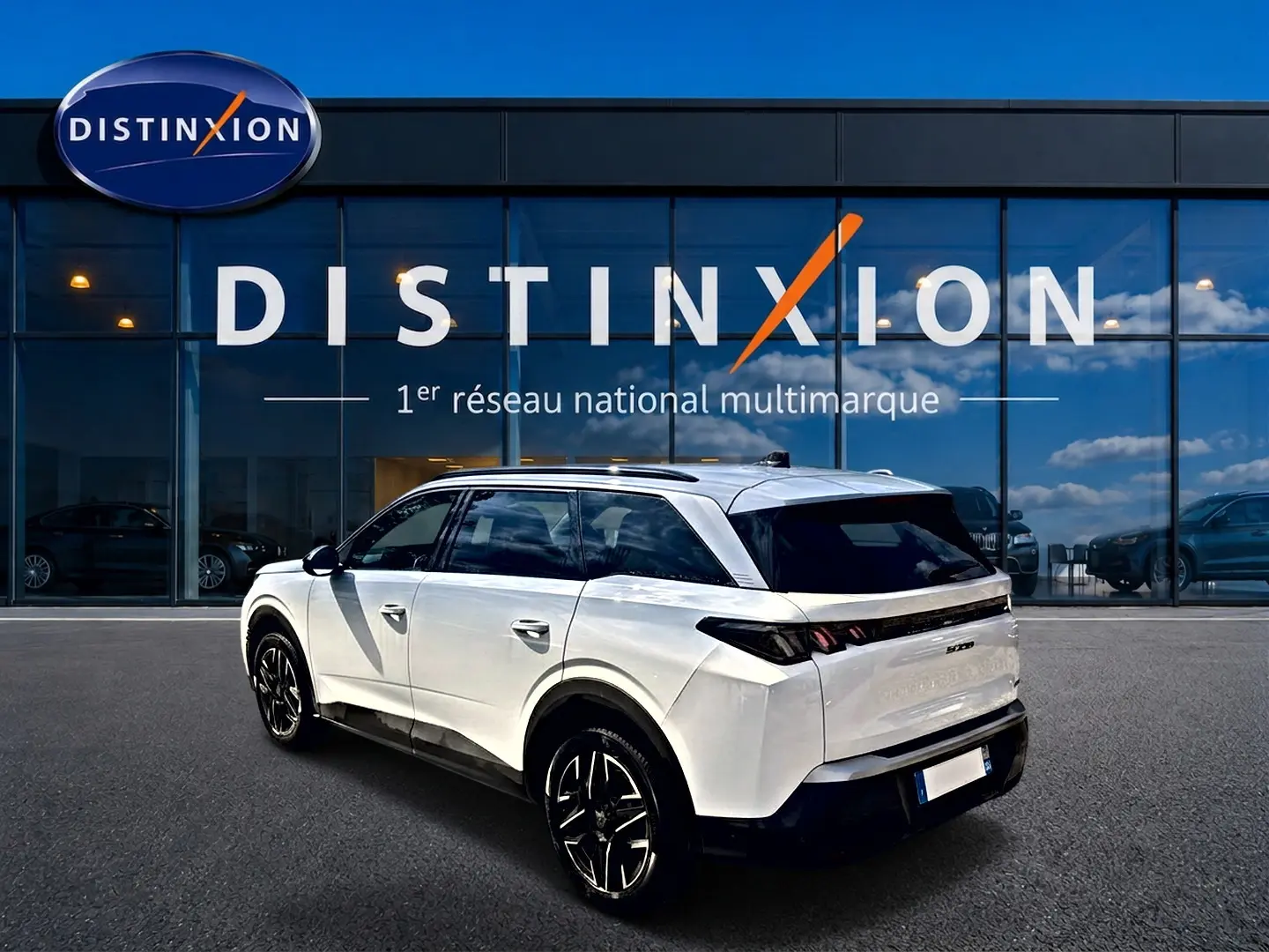 Peugeot 5008 blanc en 3/4 arrière droit, avec jantes alu noires et vitres arrière surteintées devant showroom Distinxion.