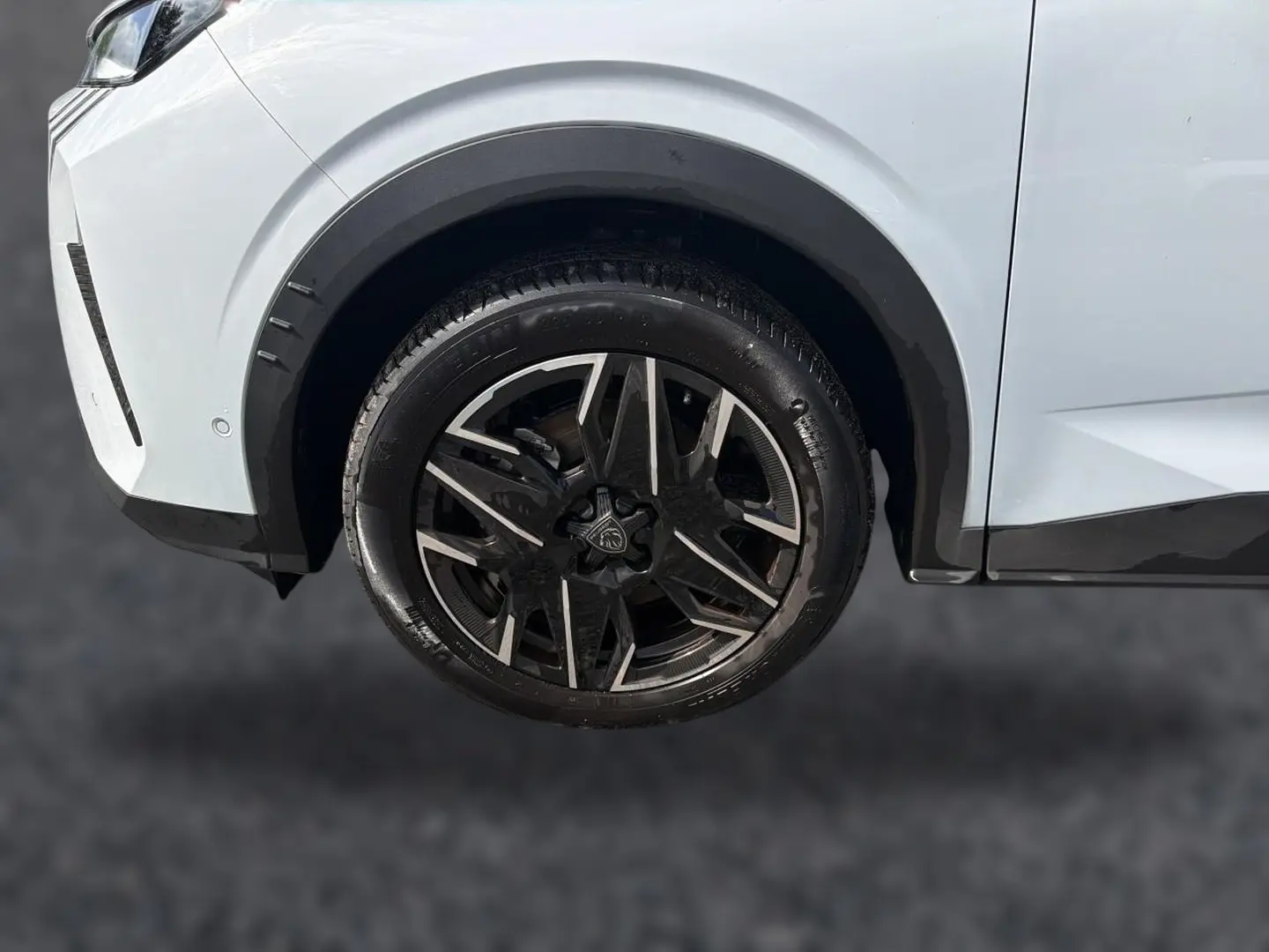 Gros plan sur la roue avant gauche avec jante alu noire et argentée du Peugeot 5008 blanc Hybrid 145 allure 2025.