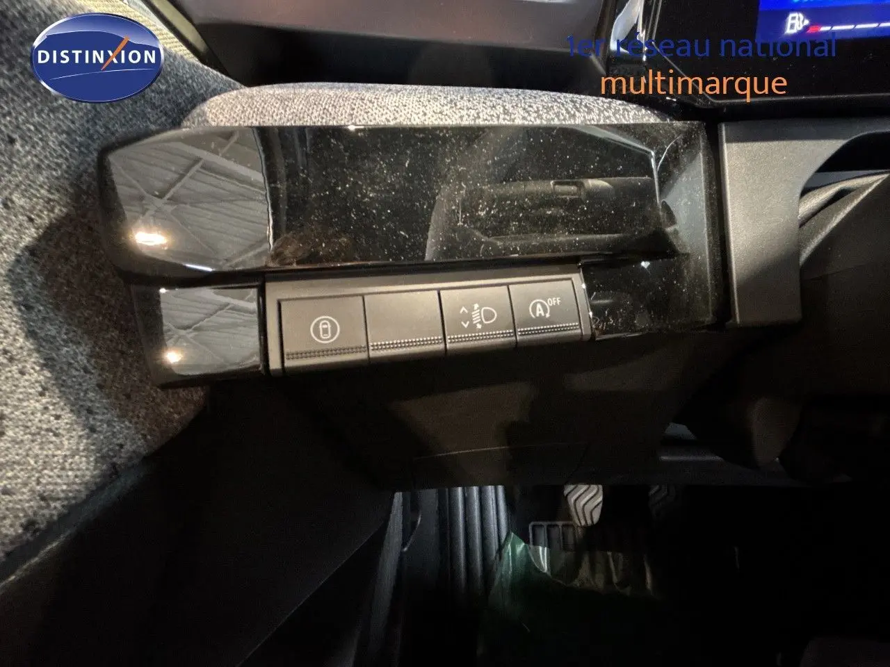 Détail intérieur montrant les commandes de réglage des phares et fonctions assistées sur une Renault Clio blanche.