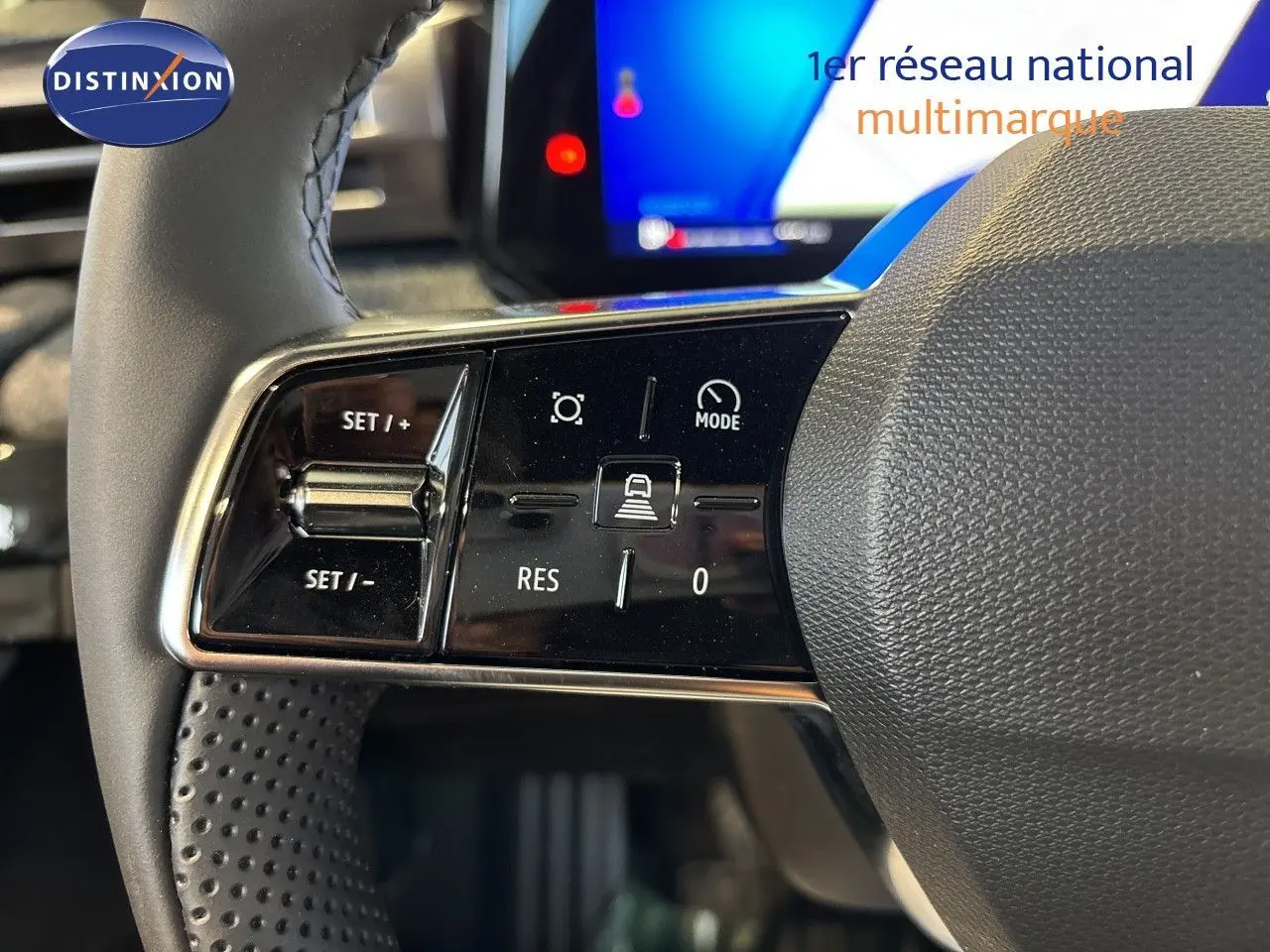 Gros plan sur les commandes à gauche du volant noir perforé de la Renault Clio VI TCe 115ch Techno, avec écran tactile en arrière-plan.