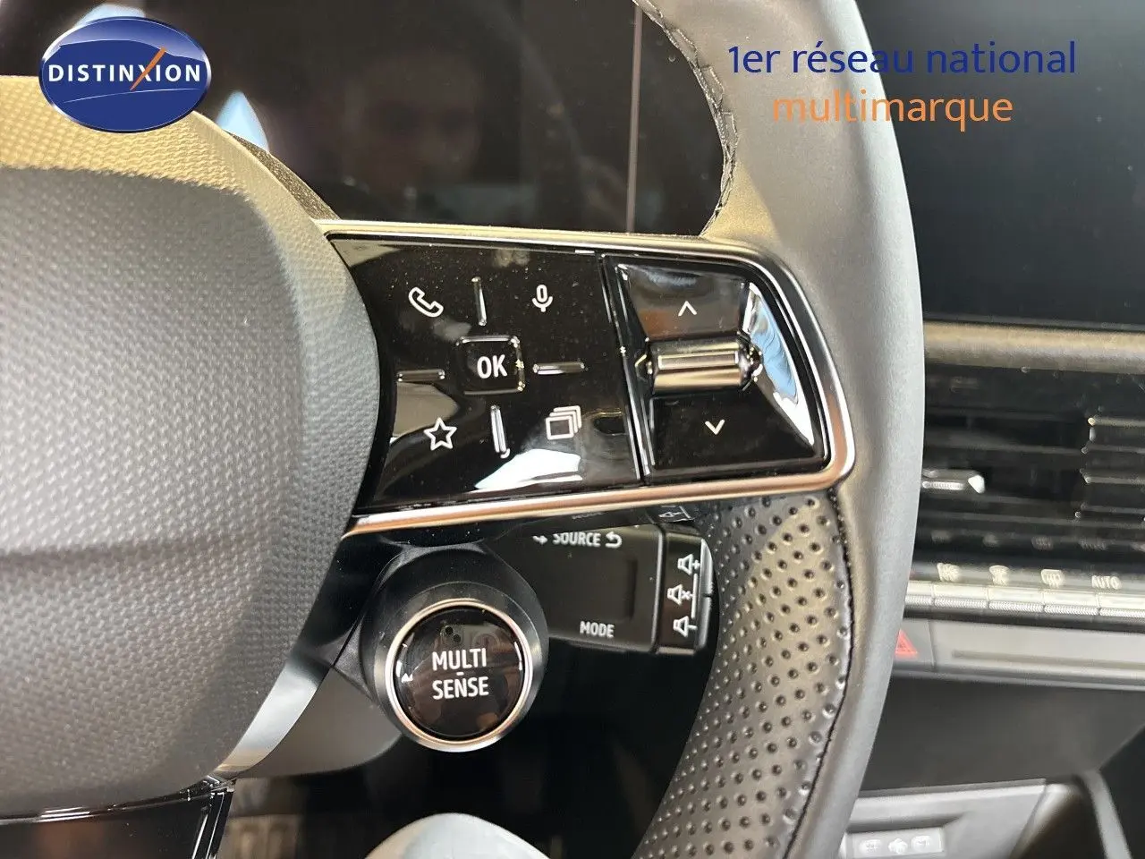 Gros plan sur le volant noir perforé de la Renault Clio blanc glacier, avec commandes multifonctions et bouton Multi Sense visible.