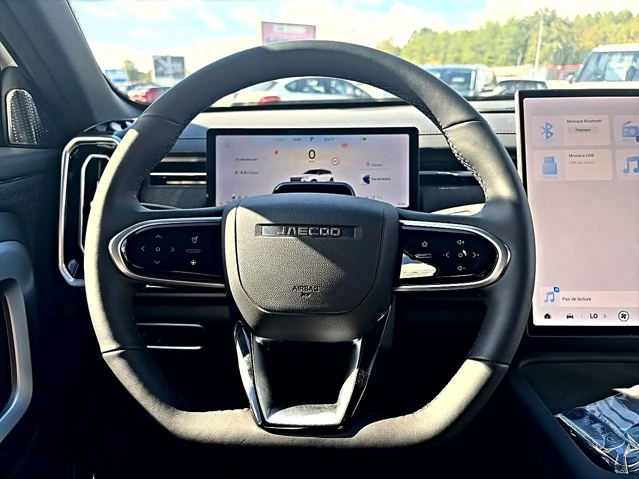 Vue intérieure centrée sur le volant noir JAECOO avec tableau de bord numérique et écran tactile latéral.