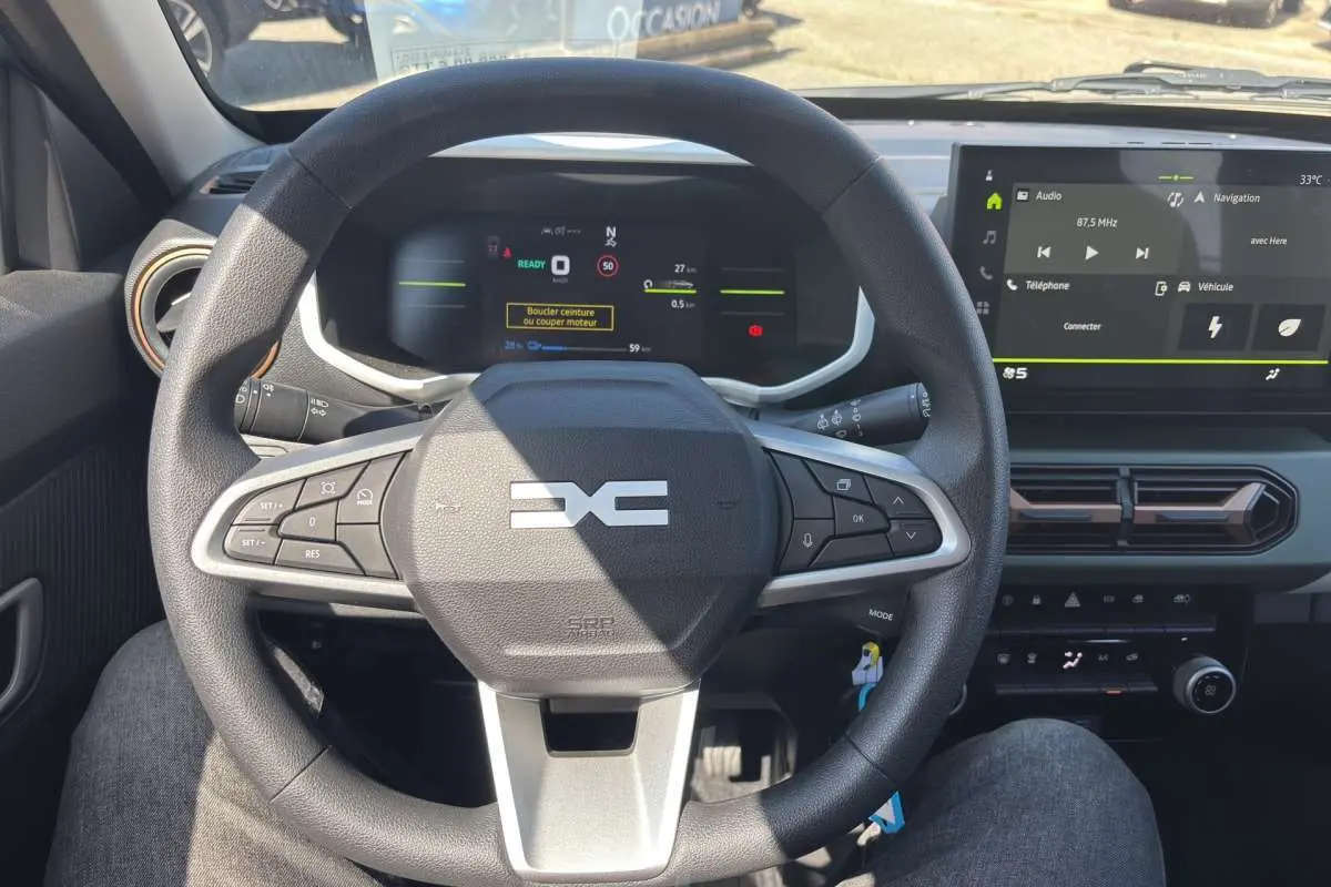 Vue intérieure centrée sur le volant DACIA Spring électrique avec tableau de bord numérique et écran tactile.
