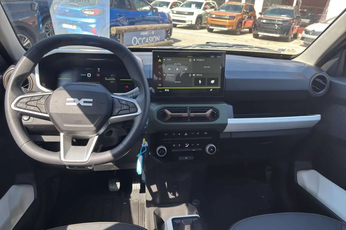 Vue intérieure du tableau de bord du Dacia Spring électrique bleu ardoise, avec écran tactile central et volant multifonction.