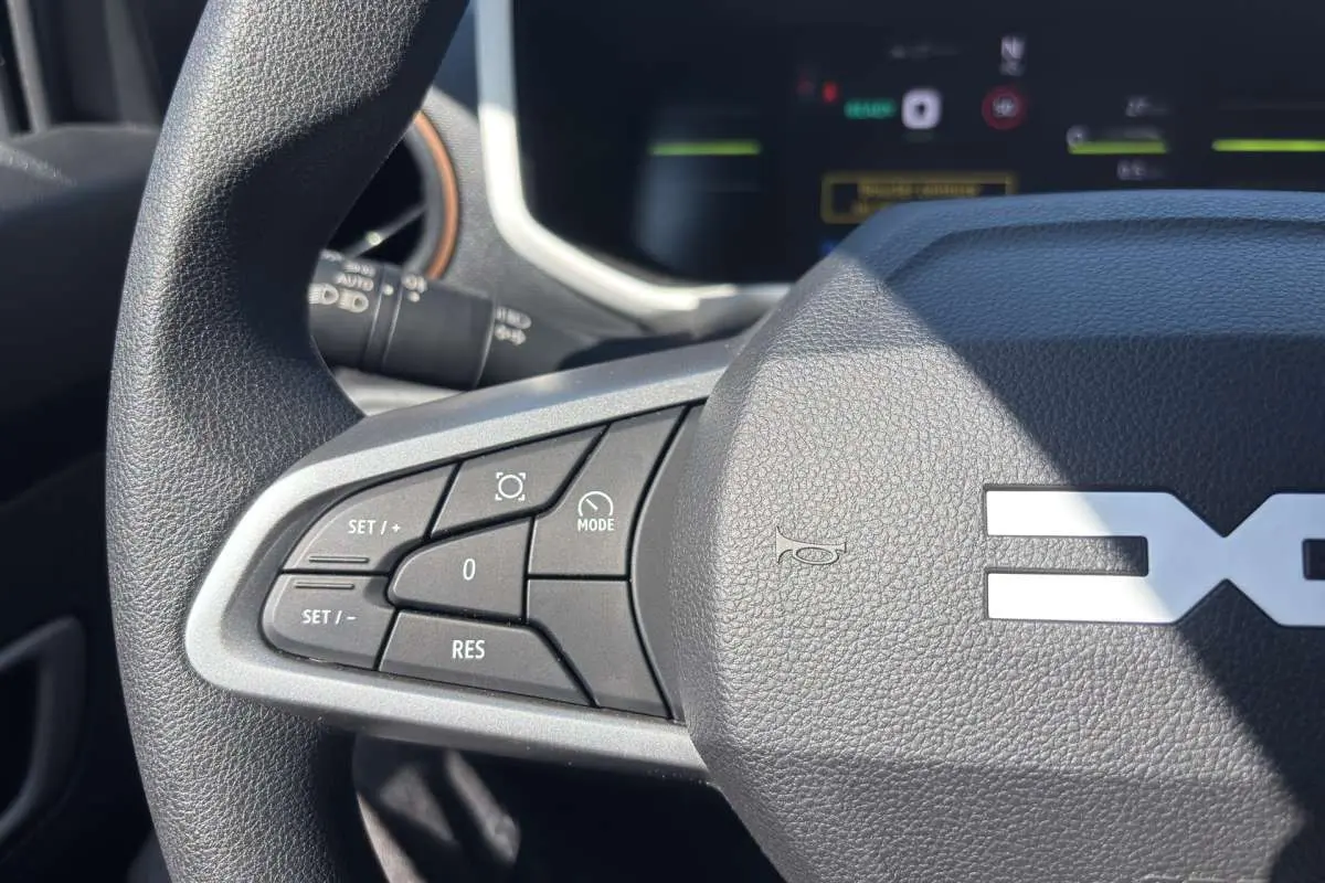 Gros plan sur le volant avec commandes multifonctions du Dacia Spring électrique 65 Extrême, intérieur noir texturé.