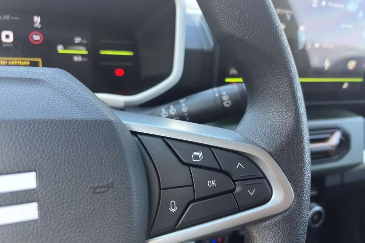 Gros plan sur les commandes au volant du Dacia Spring électrique 65 Extrême, intérieur moderne avec écran digital.