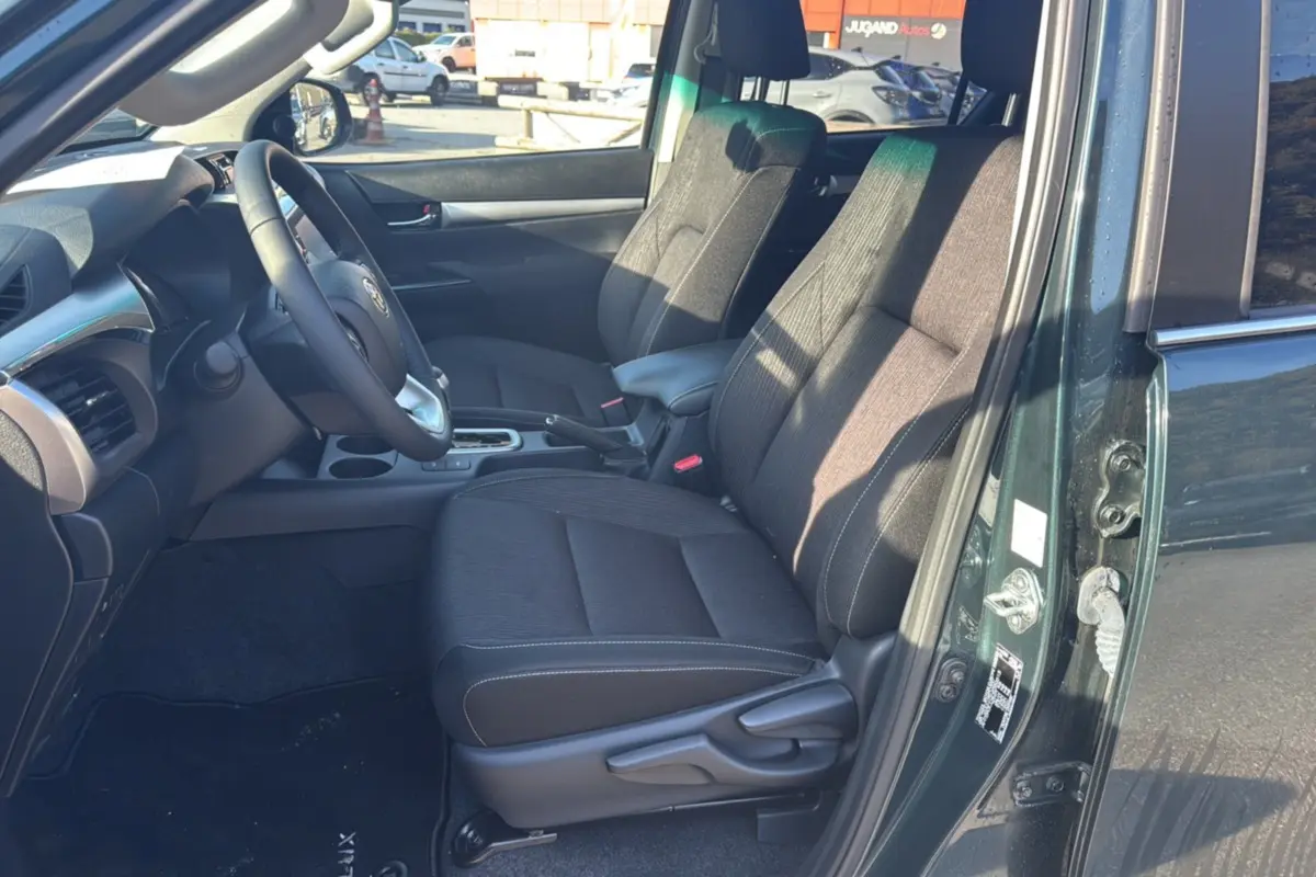 Vue intérieure côté conducteur du Toyota Hilux 2025 vert métal, montrant les sièges avant et le tableau de bord.