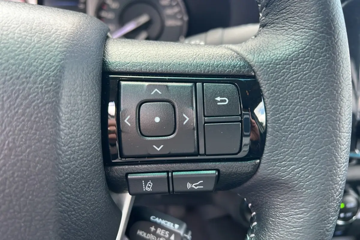 Gros plan sur les commandes multifonctions du volant en cuir noir du Toyota Hilux 4x4 vert métal 2025.