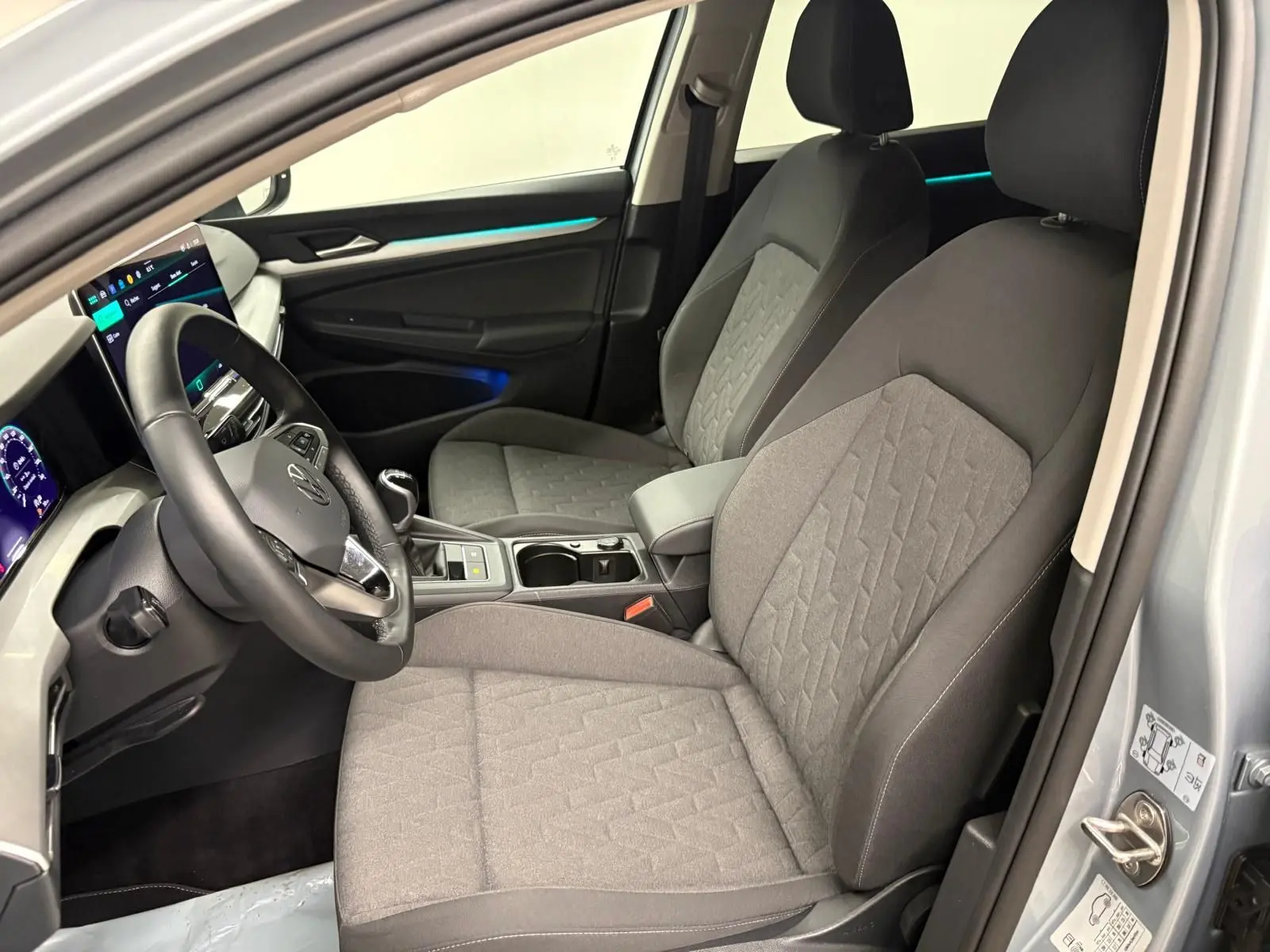 Vue intérieure côté conducteur de la Volkswagen Golf 1.5 TSI 2025 avec sièges tissu gris et éclairage d'ambiance bleu