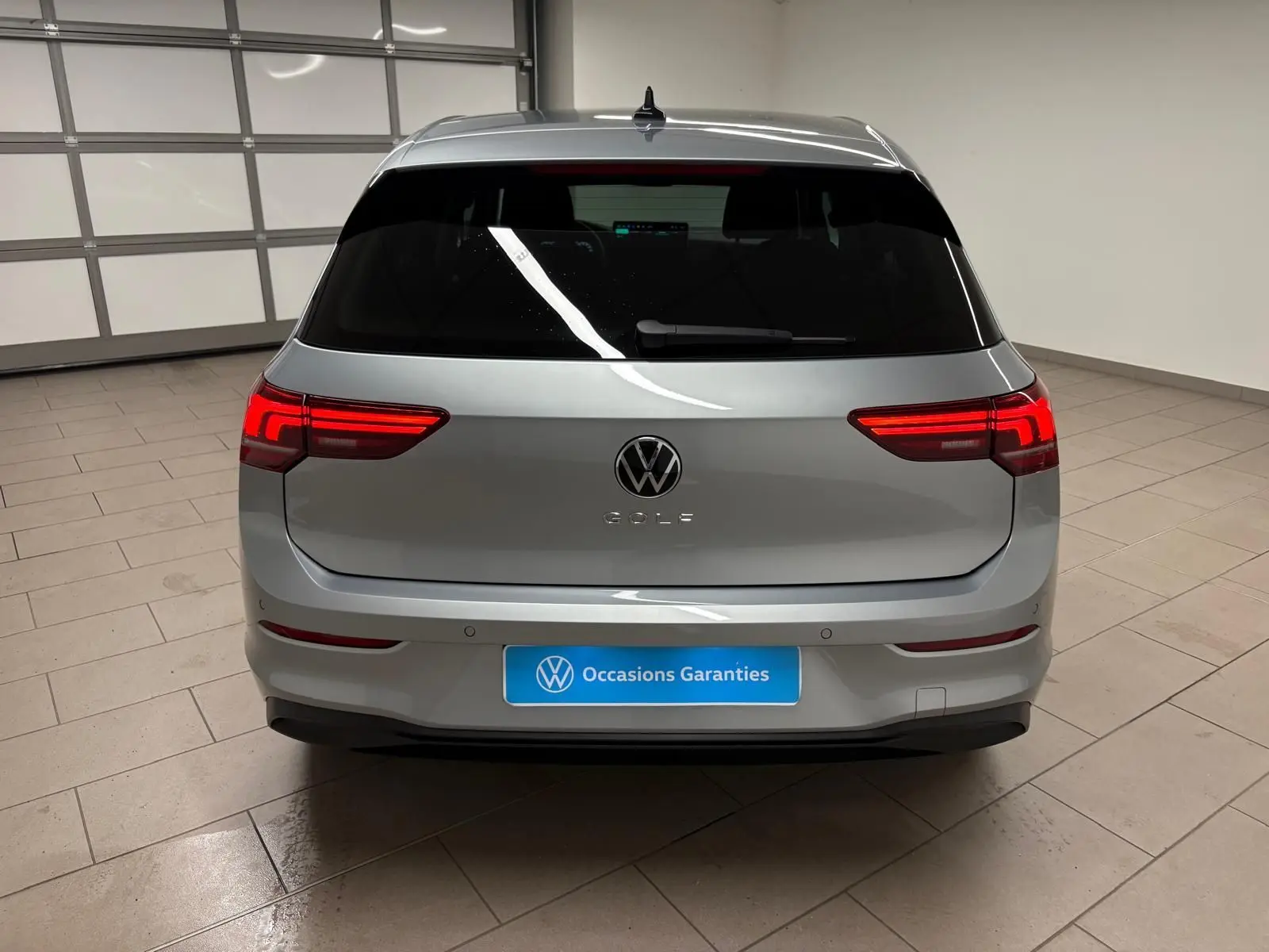 Vue arrière d'une Volkswagen Golf 1.5 TSI 116 BVM6 VW Edition en argent Dolomite avec feux LED allumés dans un garage.