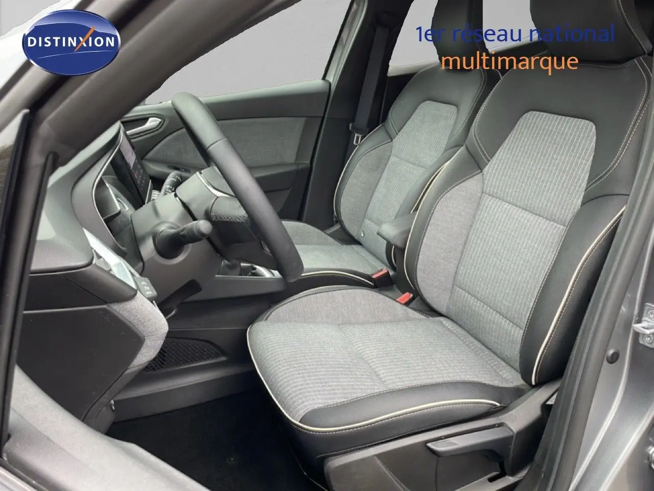 Vue intérieure côté conducteur de la Renault Clio 2025 gris schiste métal, sièges tissu gris avec surpiqûres contrastées.