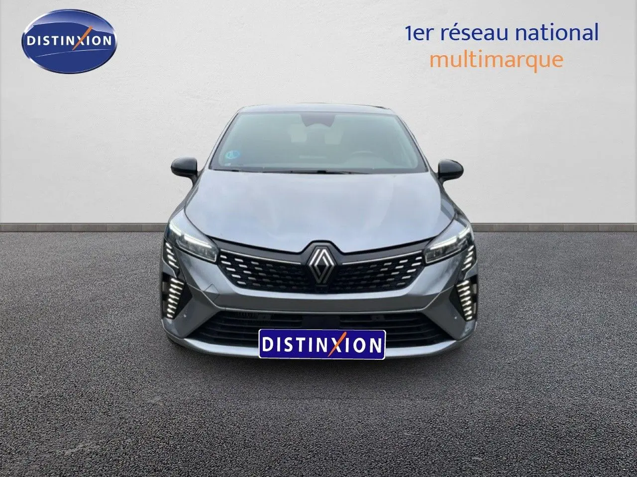 Vue de face de la Renault Clio 2025 gris schiste métal avec calandre noire et feux LED verticaux allumés.