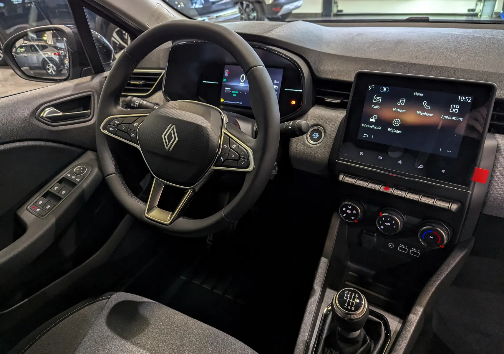 Vue intérieure côté conducteur de la Renault Clio V Gris Rafale, avec volant multifonction et écran tactile central allumé.