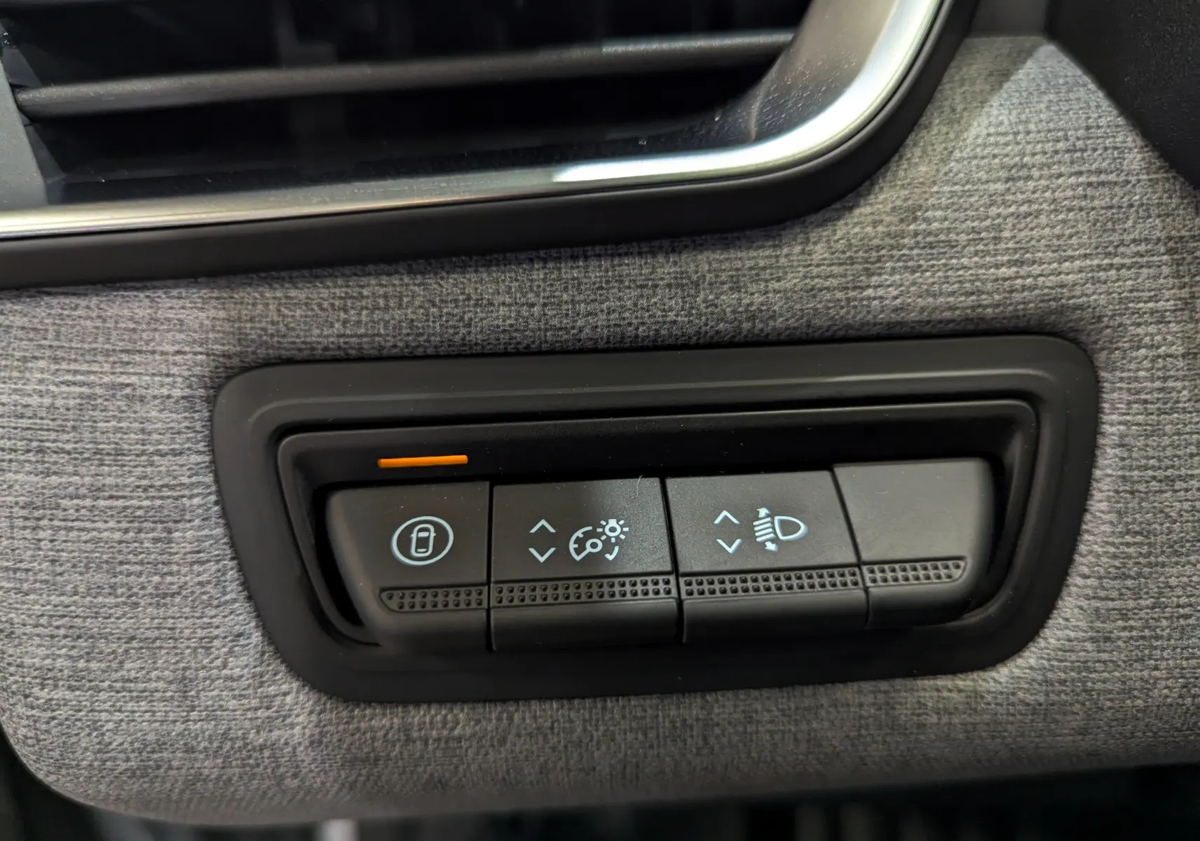 Gros plan sur les commandes de réglage des phares et verrouillage, intérieur tissu gris de la Renault Clio V 2025.