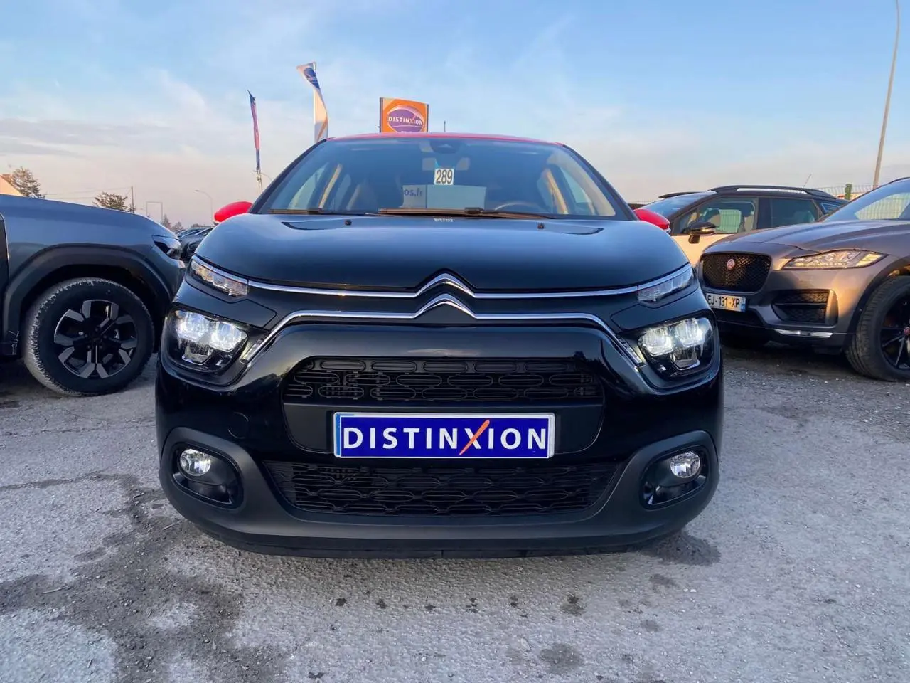 Vue avant d'une Citroën C3 Shine 2023 noire avec toit rouge et feux LED allumés sur parking.
