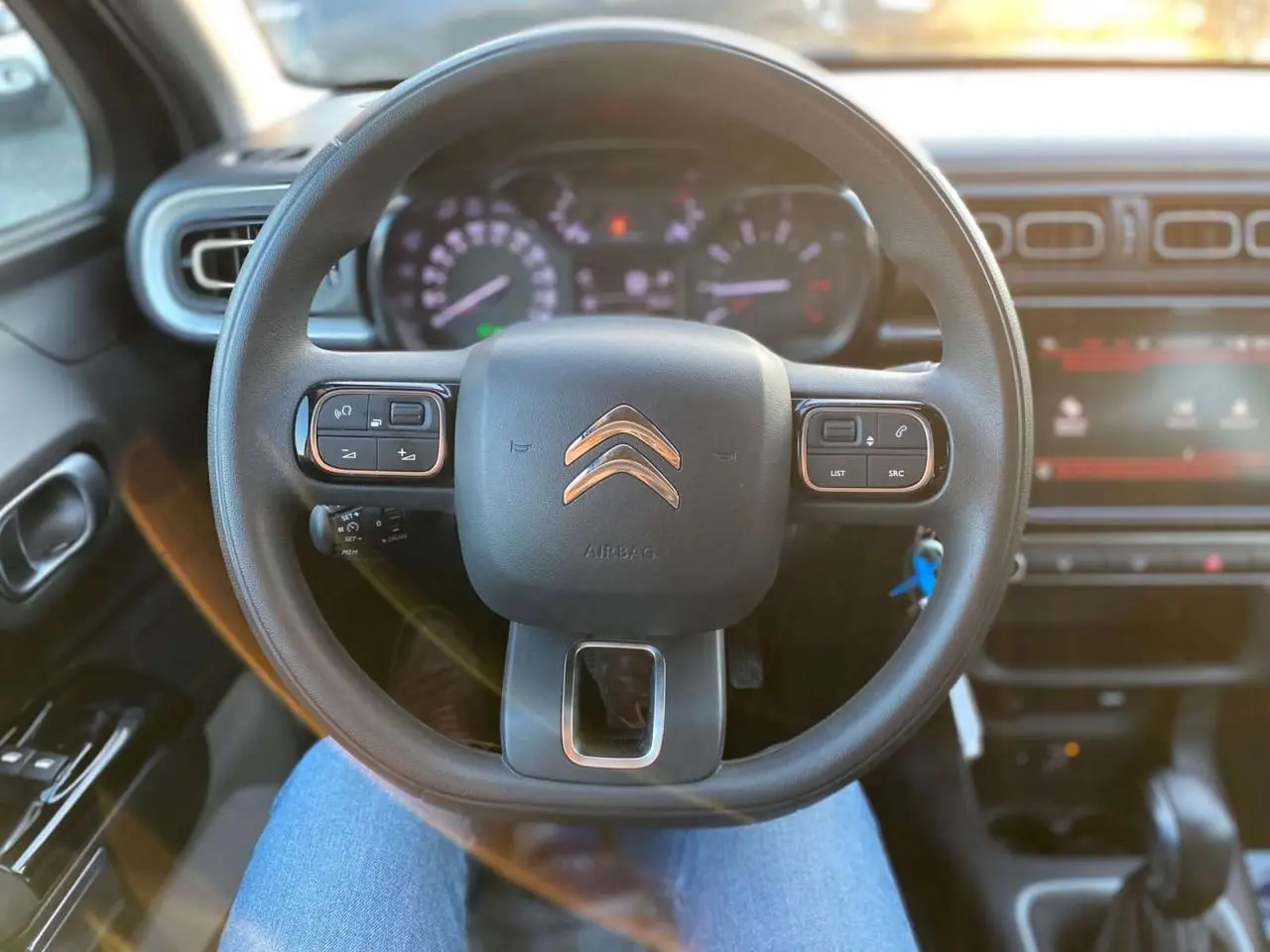 Vue centrée sur le volant du Citroën C3 Shine 2023, avec commandes audio intégrées et tableau de bord flou en arrière-plan.