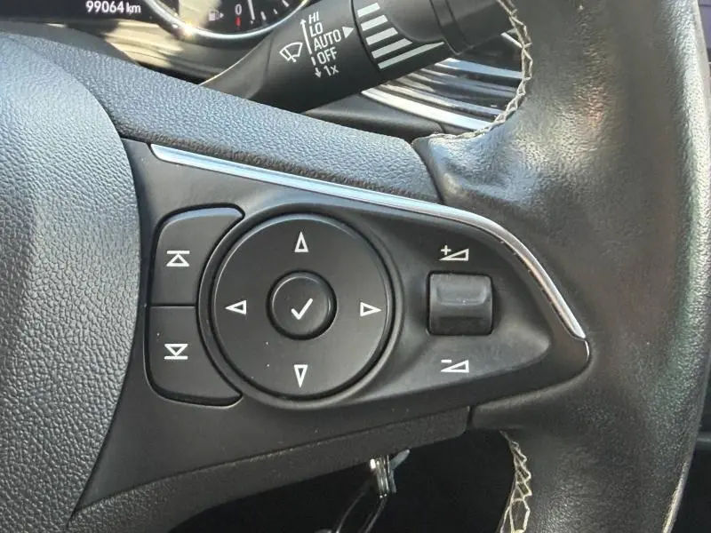 Gros plan sur les commandes multifonctions noires du volant en cuir de l'Opel Insignia Grand Sport brun Carbone, côté gauche.