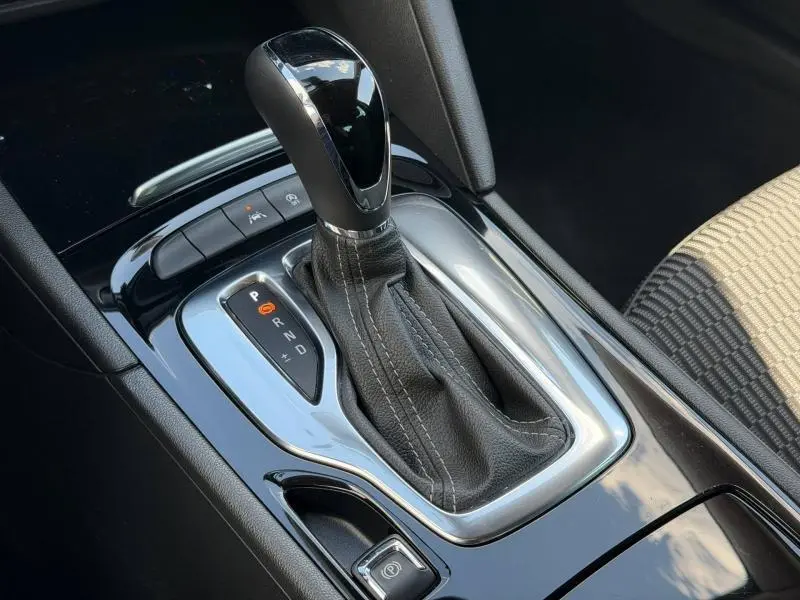 Gros plan sur le levier de vitesse automatique noir et chrome de l’Opel Insignia Grand Sport, avec sellerie tissu beige visible.