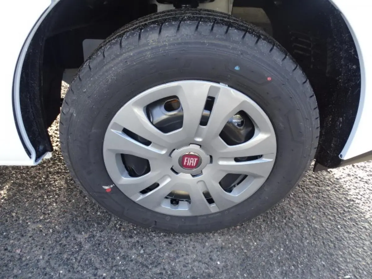 Gros plan sur la roue avant droite d’un Fiat Talento blanc avec enjoliveur gris et logo rouge FIAT.