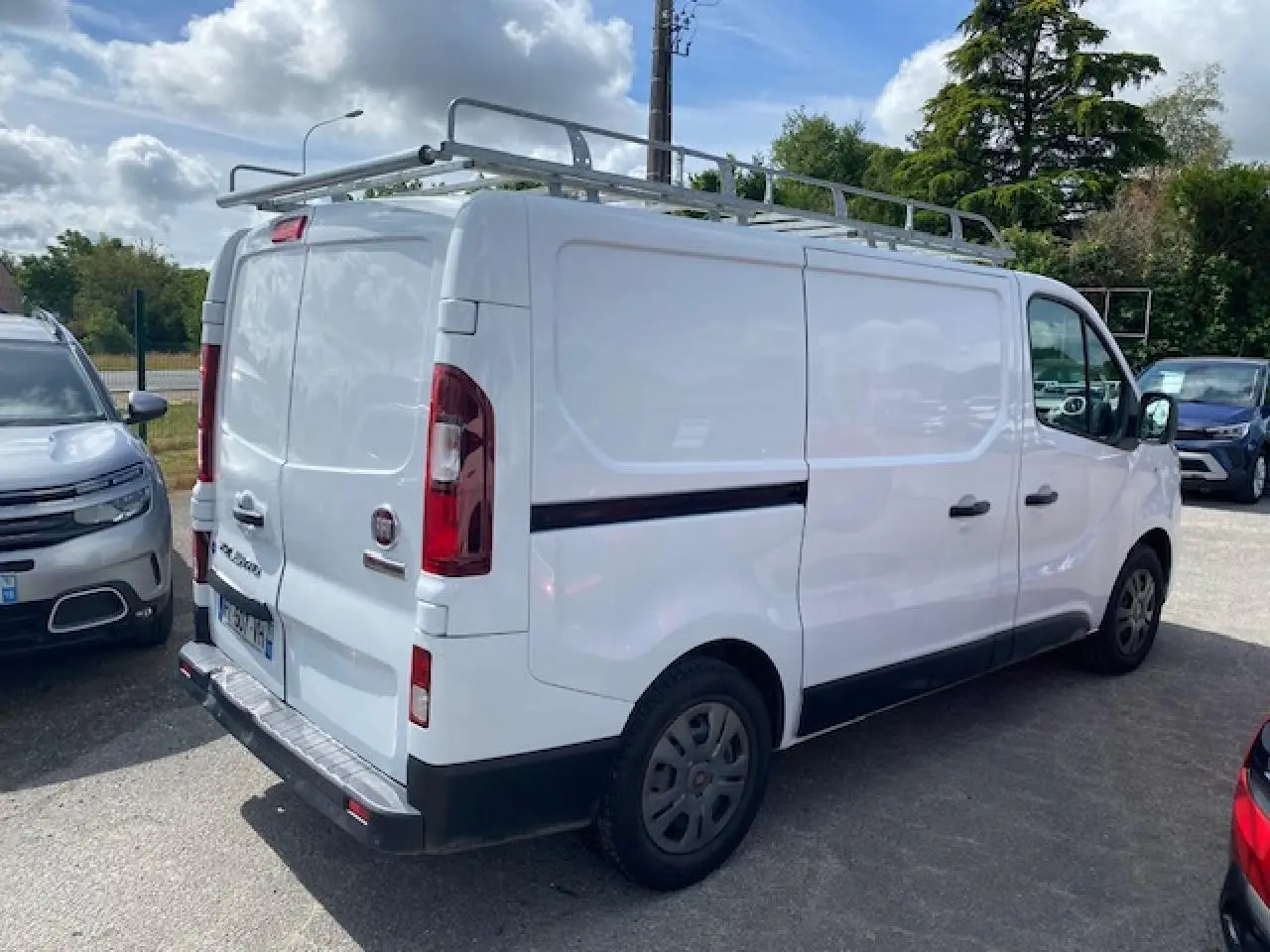 Fiat Talento Fourgon blanc vu en 3/4 arrière droit avec galerie de toit et portes arrière tôlées ouvertes à 180°.